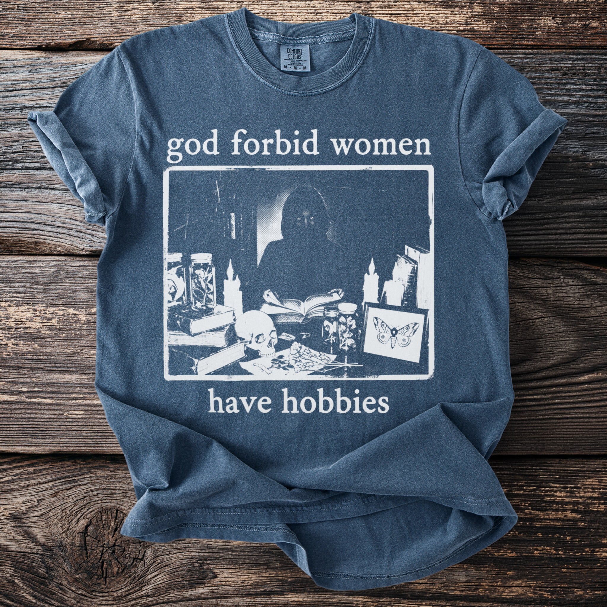Blue t-shirt with "god forbid women have hobbies" text and an illustration.