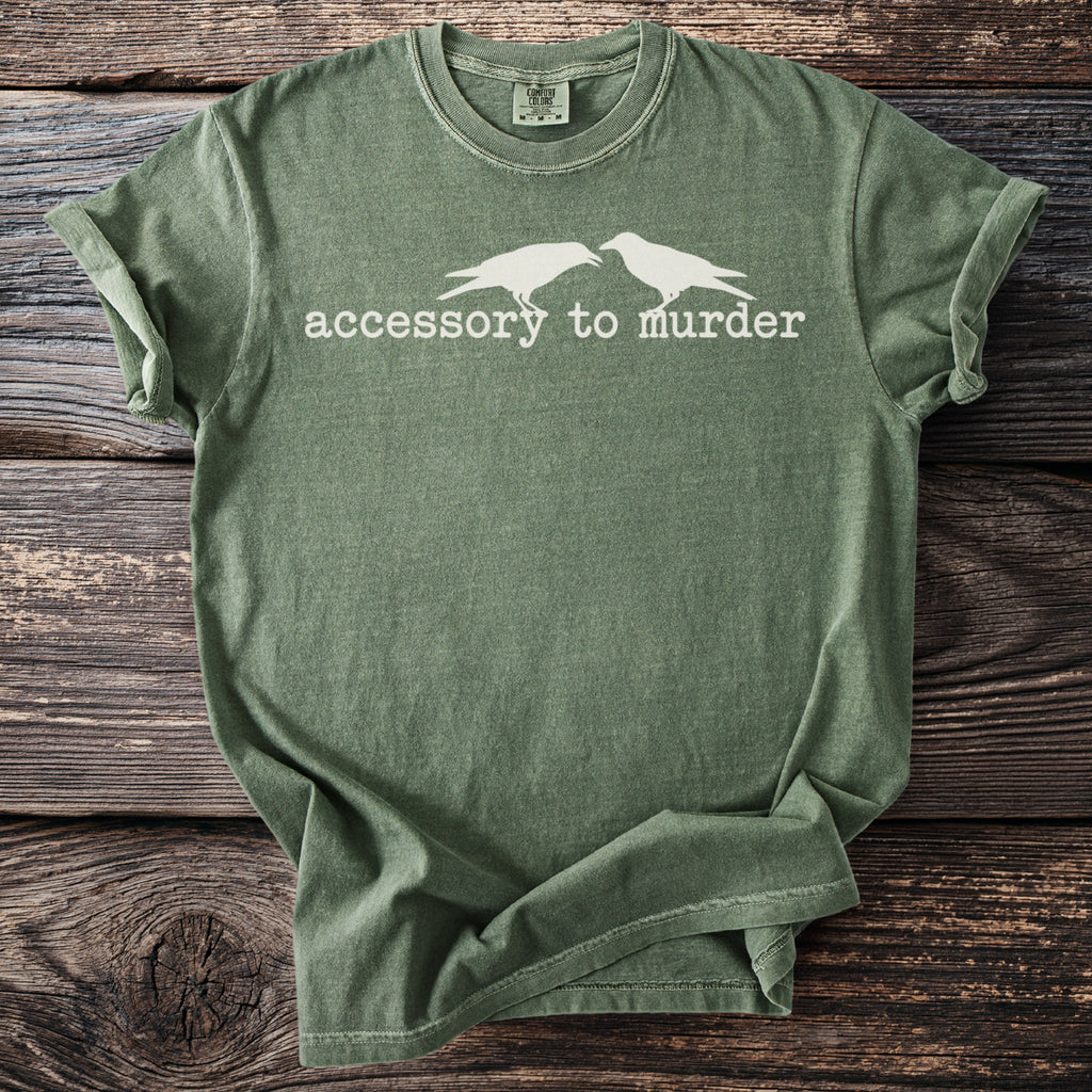 Olive green t-shirt with white crows and text reading "accessory to murder".