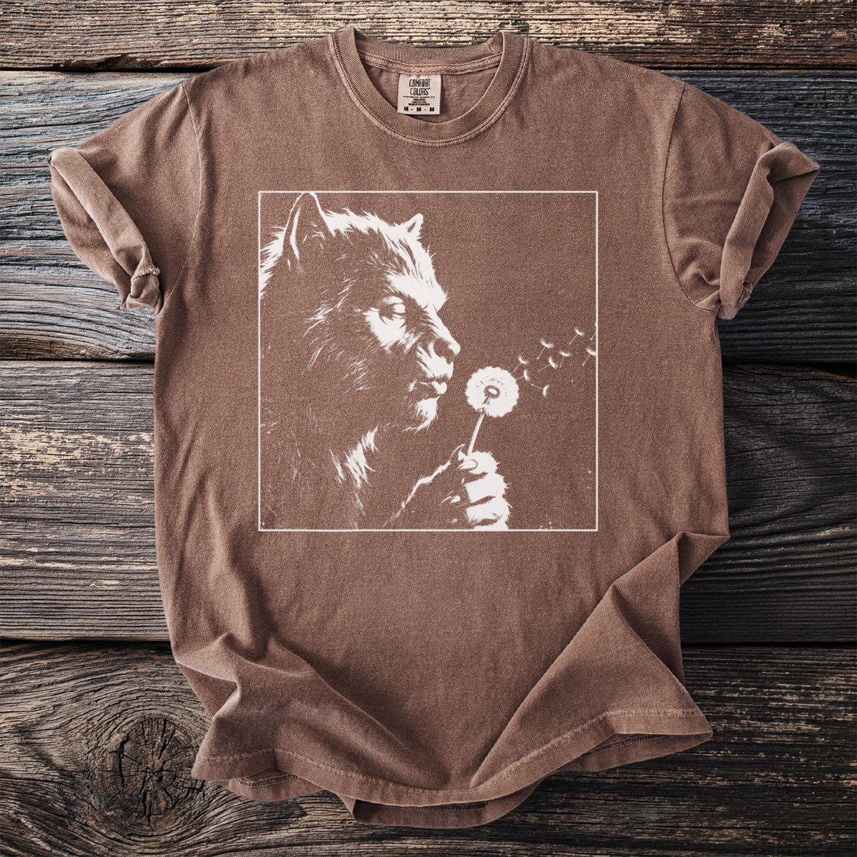 Brown t-shirt with white graphic of a werewolf blowing on a dandelion.