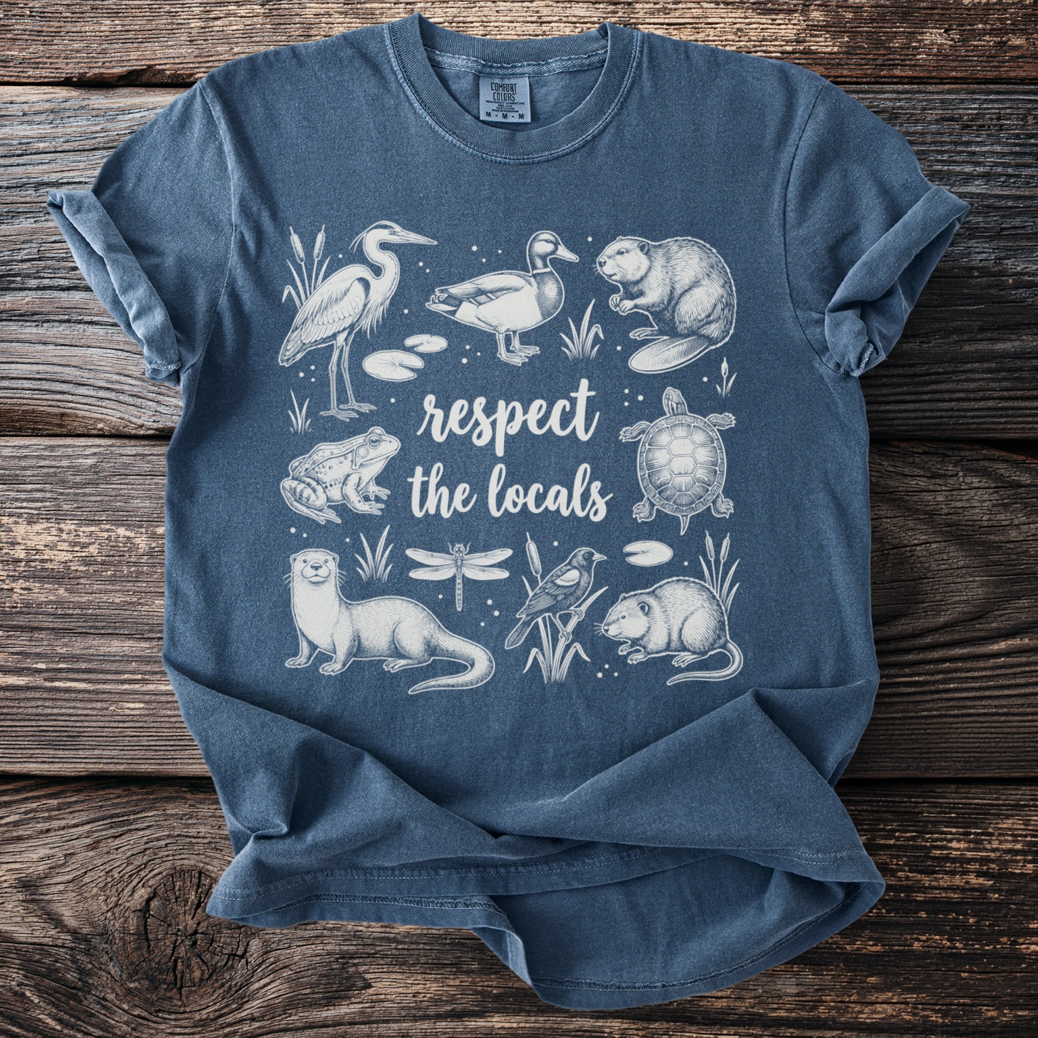 Blue t-shirt with white line art of marsh animals and the words "respect the locals."