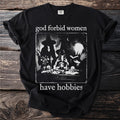 Black t-shirt with "god forbid women have hobbies" graphic featuring witches and occult items.