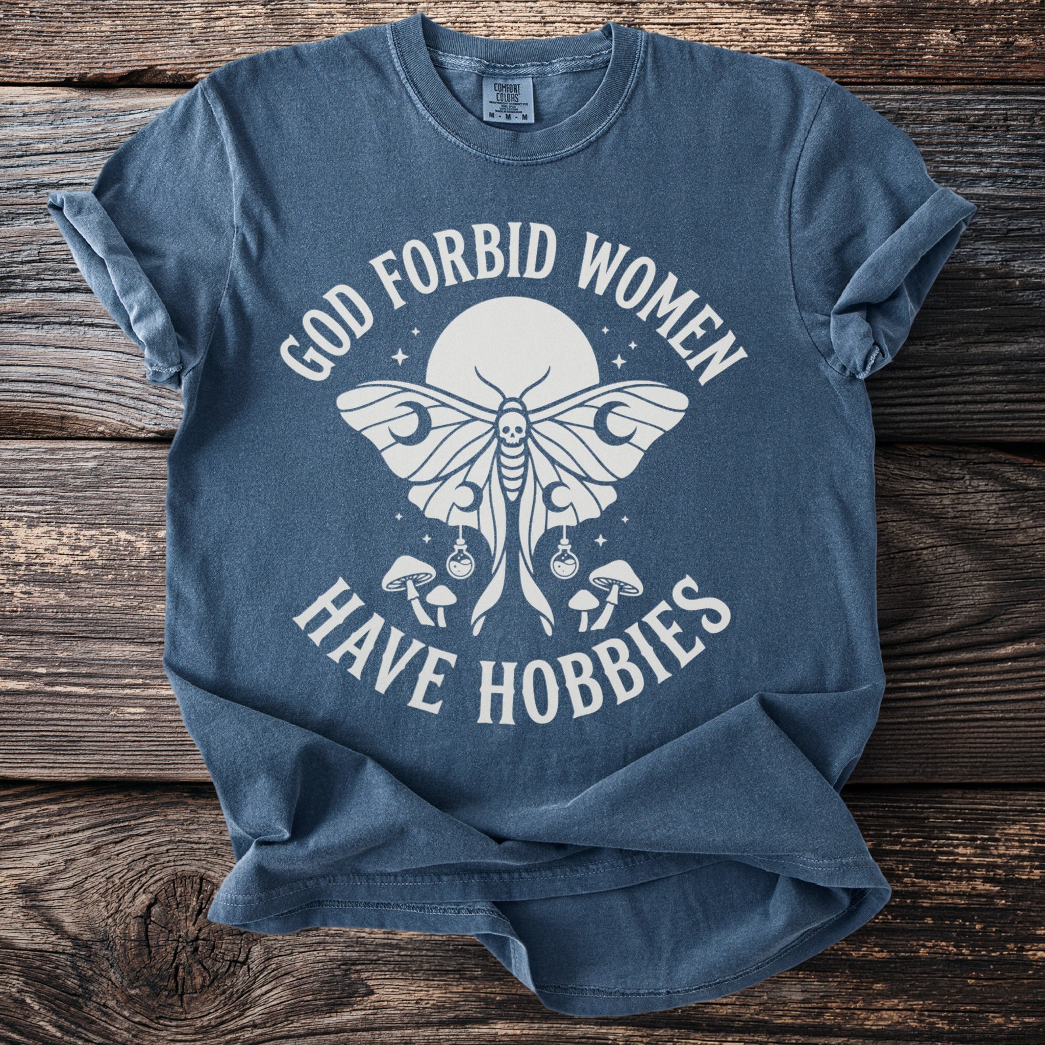 Blue t-shirt with moth, mushrooms, and text: "God Forbid Women Have Hobbies."