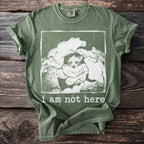 Green t-shirt with a distressed print of a dog peeking from laundry, saying "i am not here".