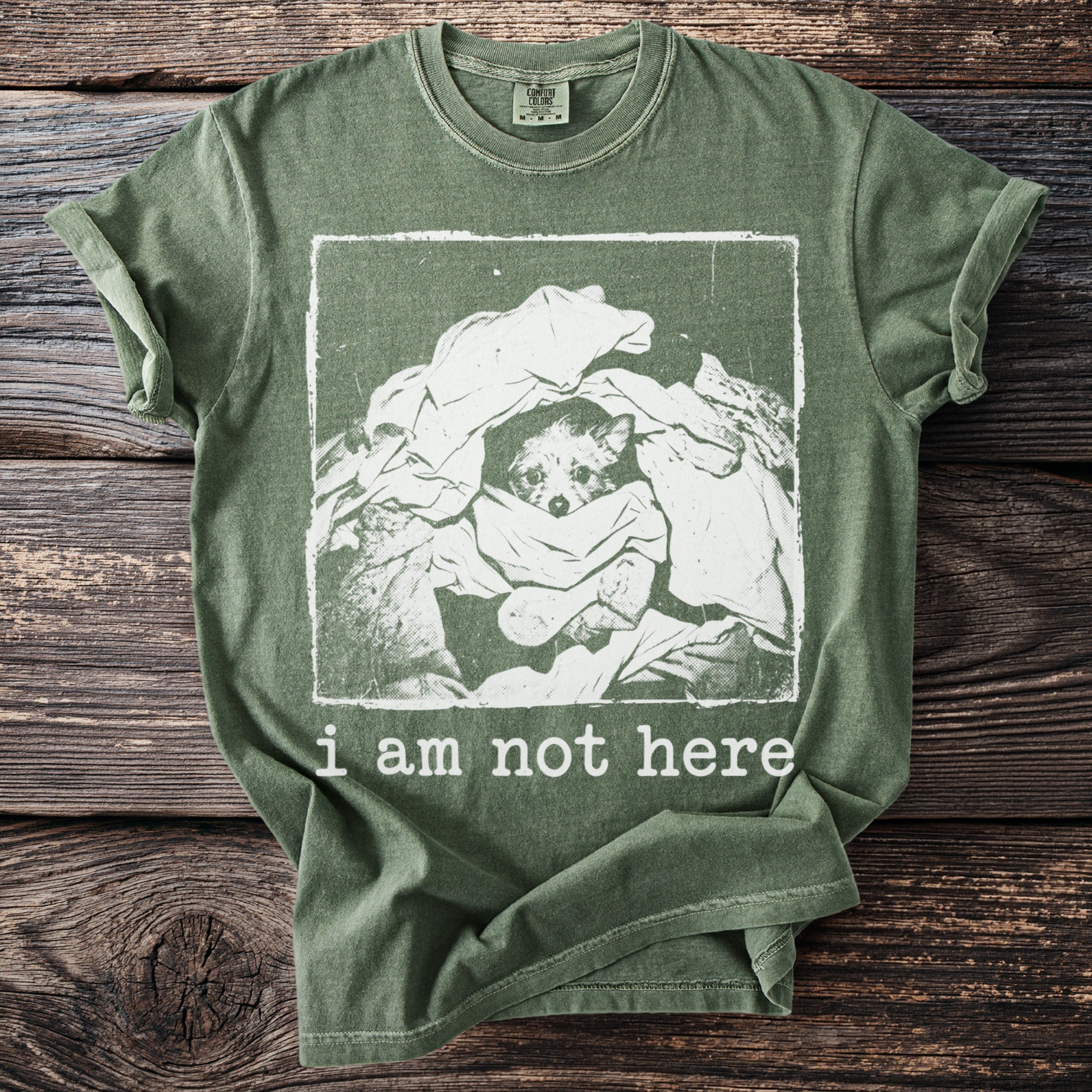 Green t-shirt with a distressed print of a dog peeking from laundry, saying "i am not here".