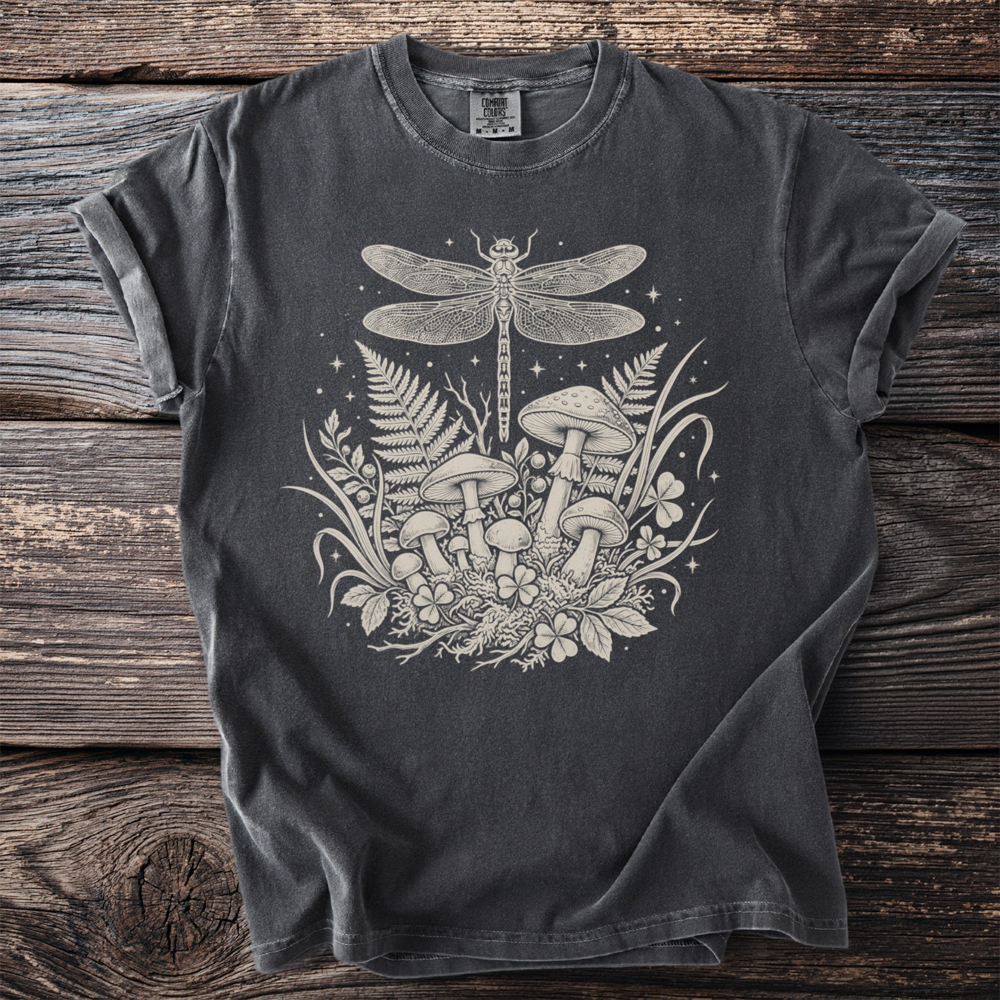 T-shirt with a cream-colored print of a dragonfly, mushrooms, ferns, and clover.