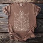 Brown t-shirt with a print of a crowned woman, ravens, bones, and flowers.