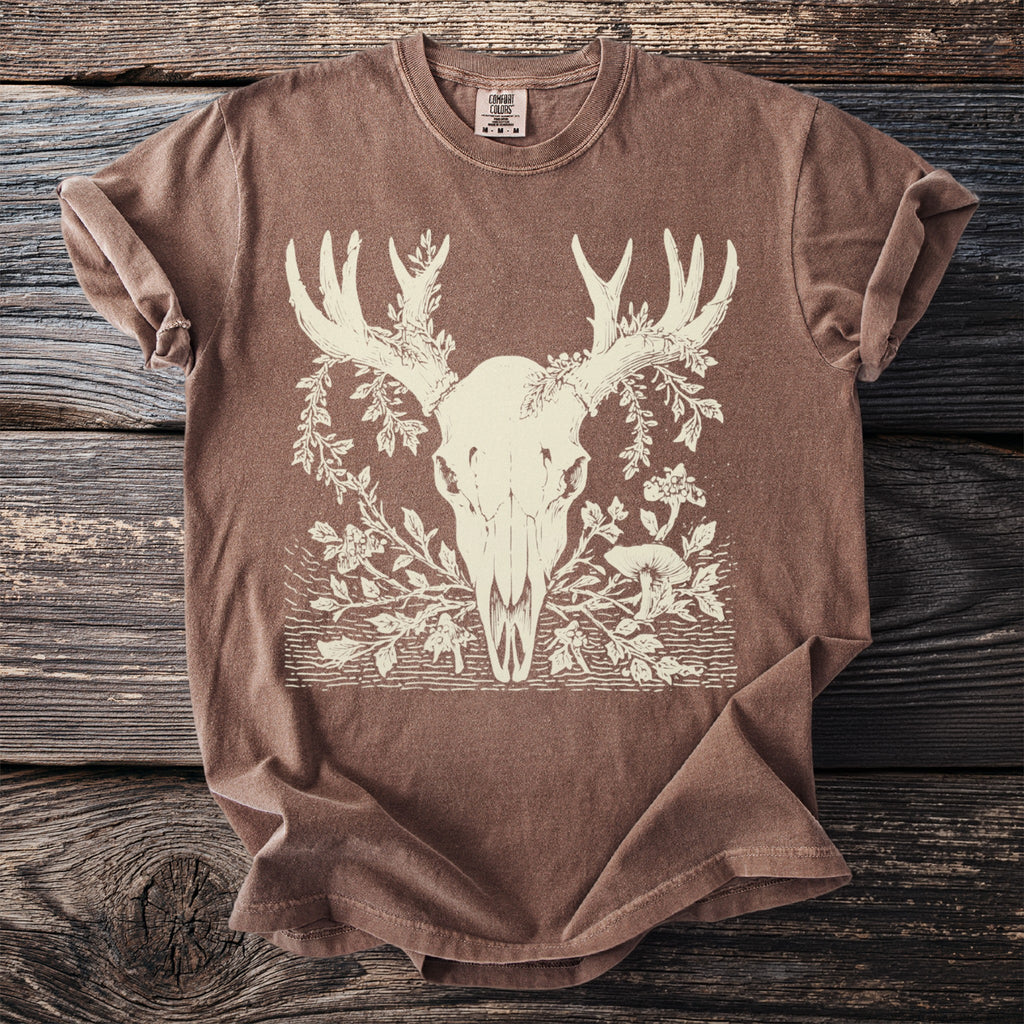 Brown t-shirt with cream line art of deer skull, antlers, foliage, and mushrooms.