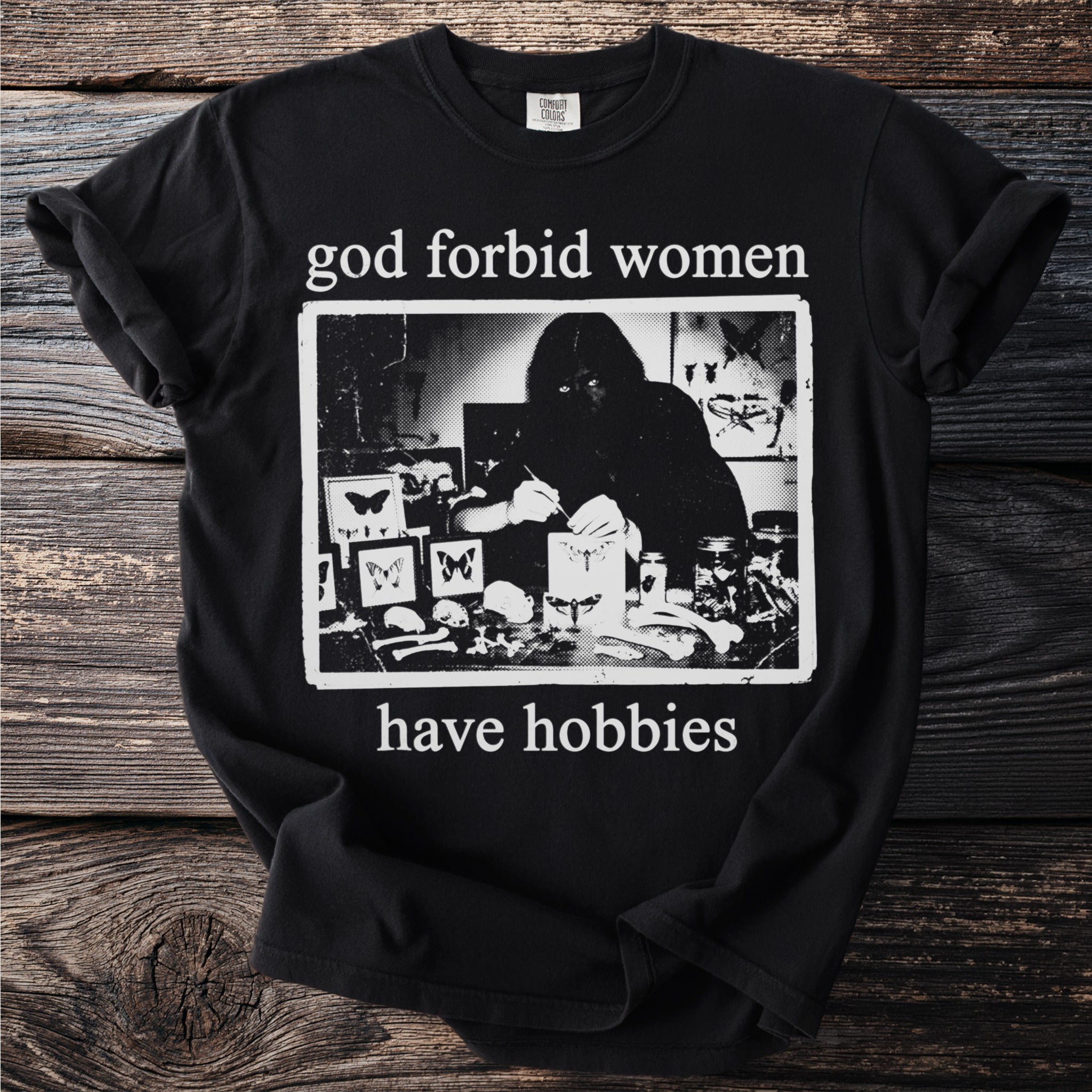 Black t-shirt with "god forbid women have hobbies" text and an illustration of a person with butterflies and skulls.