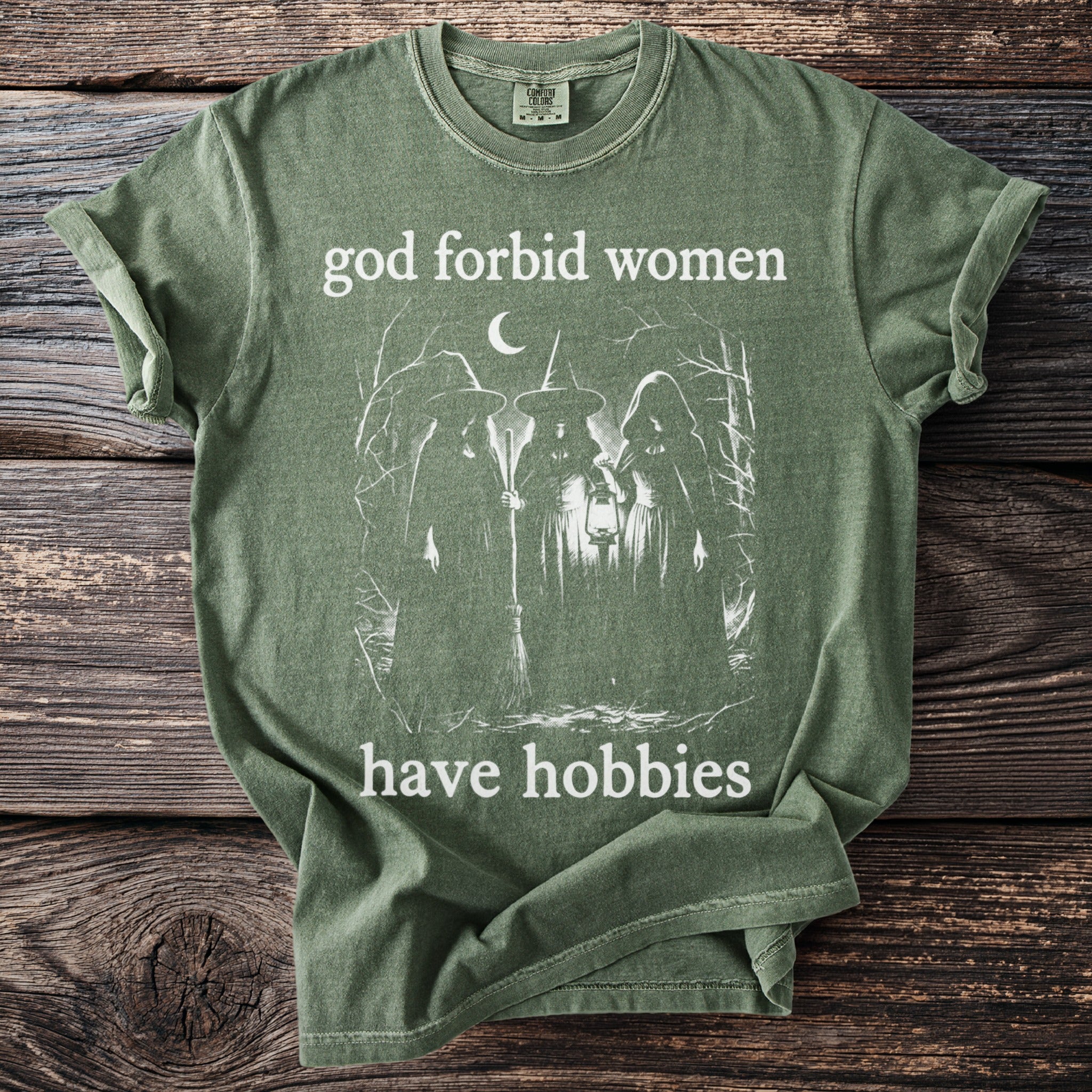 Green t-shirt with "god forbid women have hobbies" and three witches graphic.