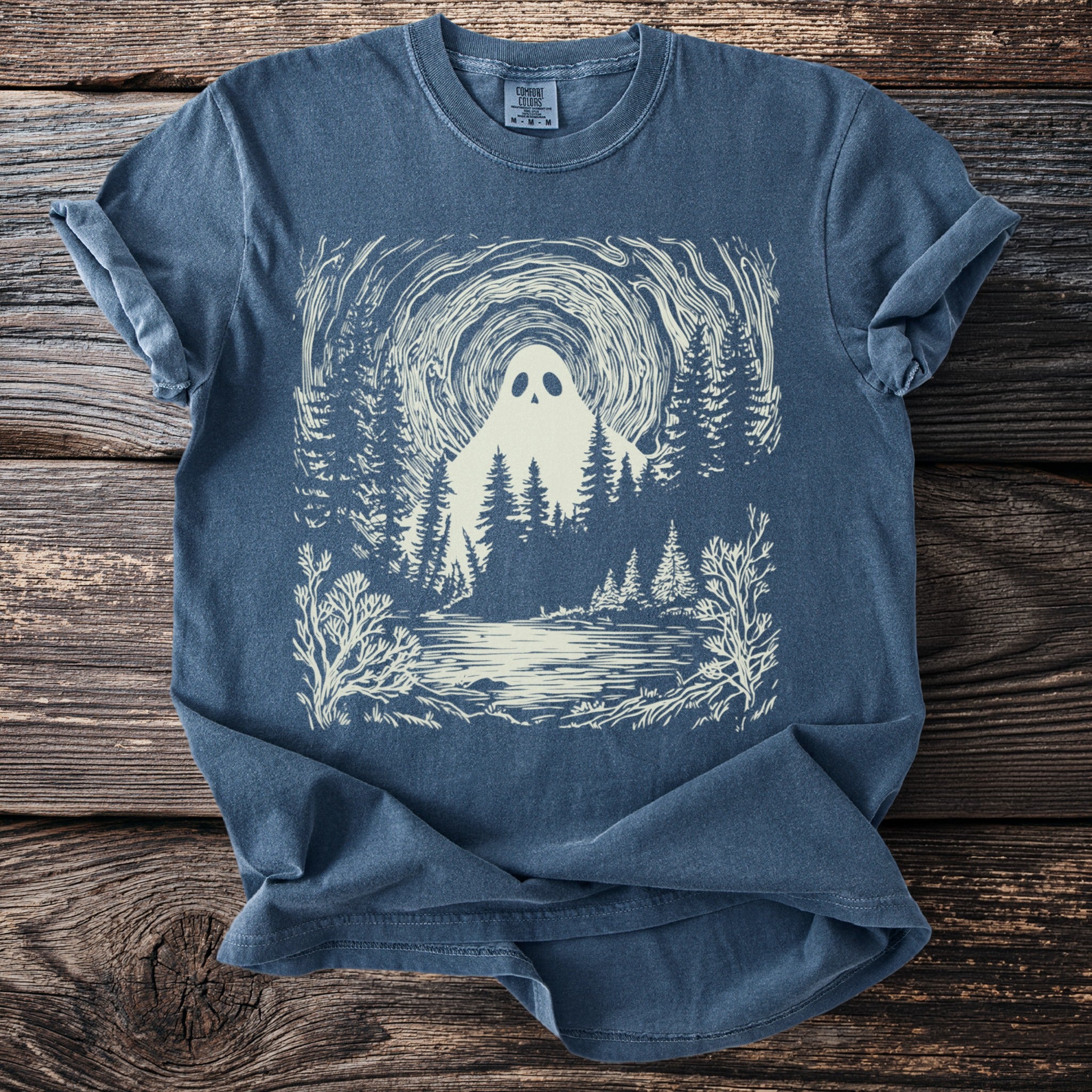 Blue t-shirt with a cream illustration of a ghost in a forest by a lake.