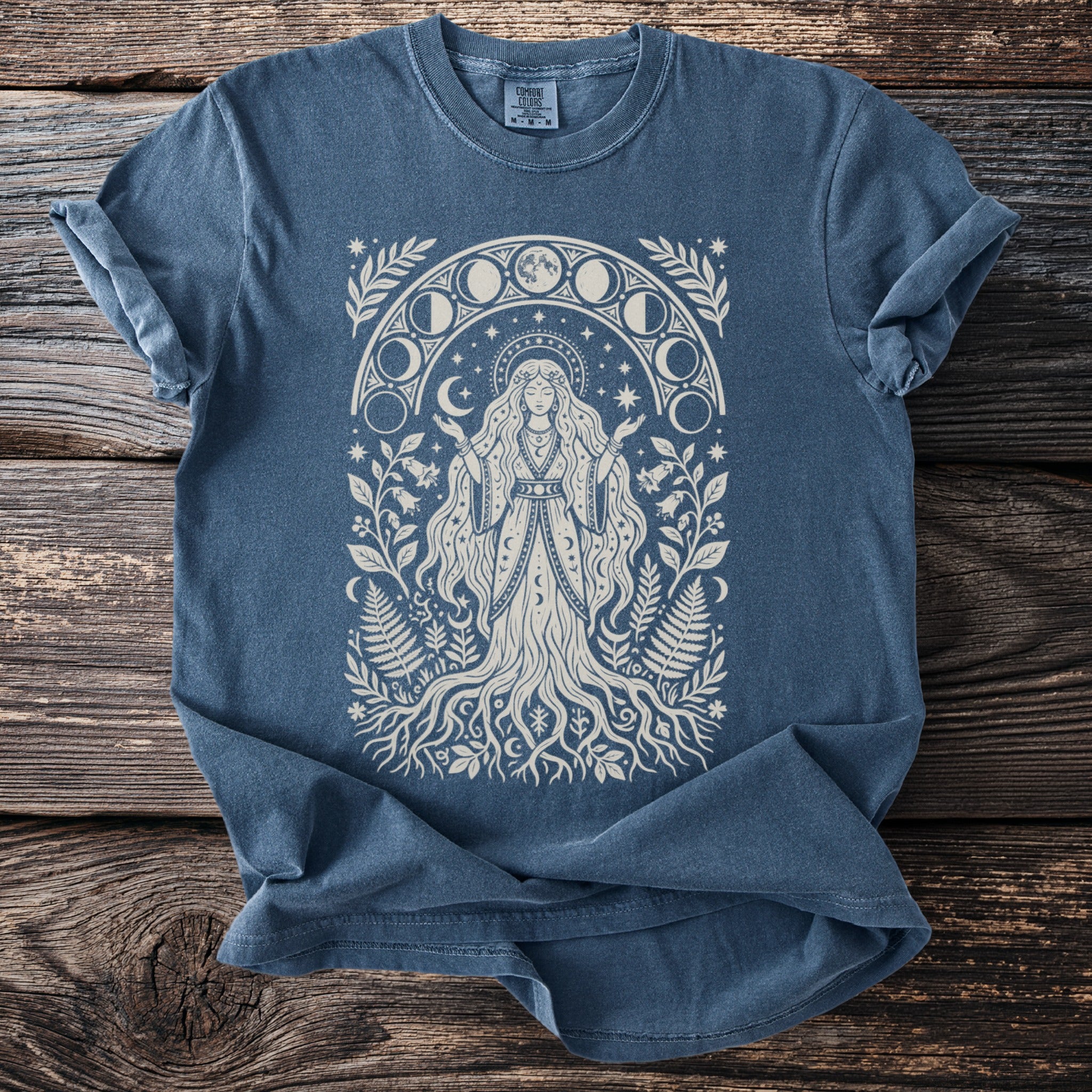 Blue t-shirt with a cream-colored graphic of a woman surrounded by moon phases and foliage.