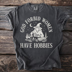 Dark gray t-shirt with "GOD FORBID WOMEN HAVE HOBBIES" text and witch graphic.