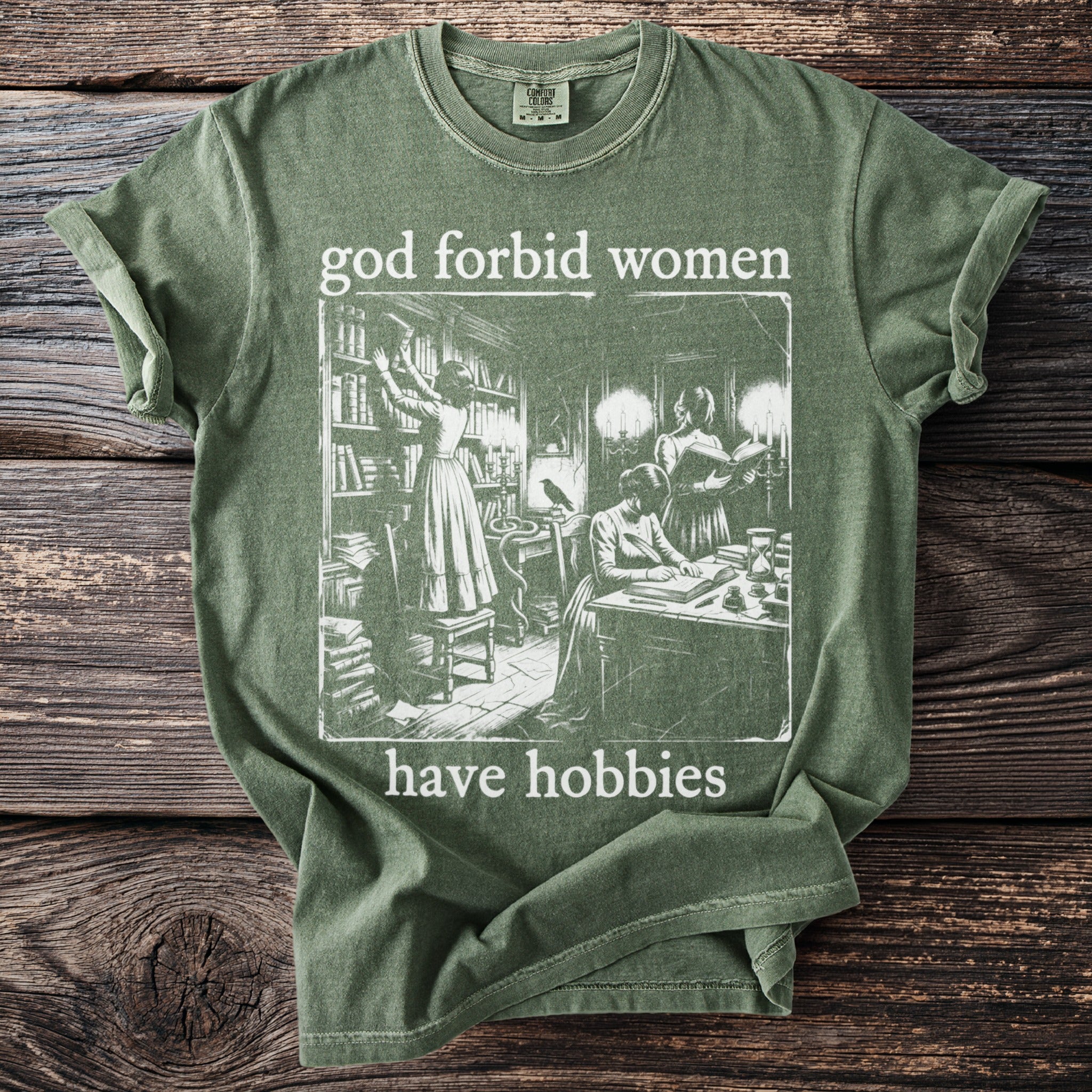 Green t-shirt with "god forbid women have hobbies" text and vintage library illustration.