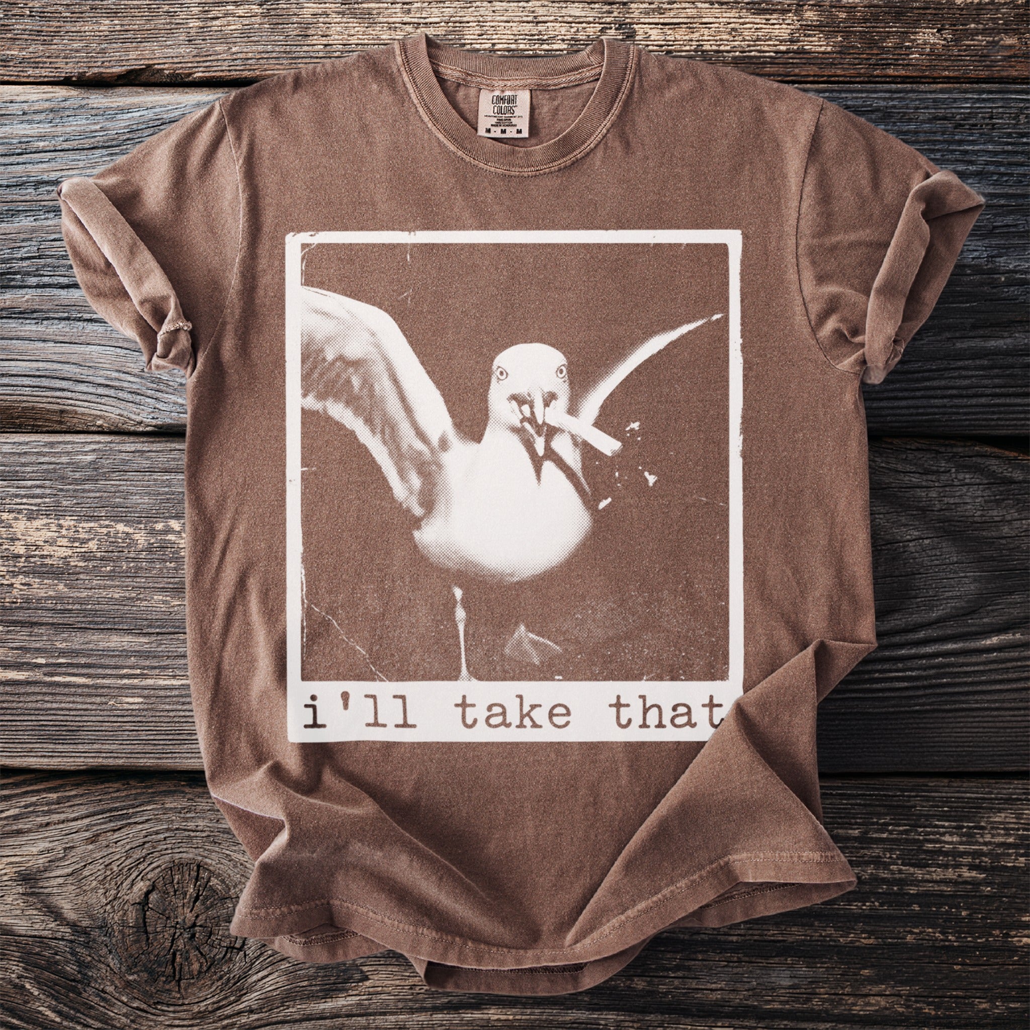 Brown t-shirt with a seagull graphic and text "i'll take that".