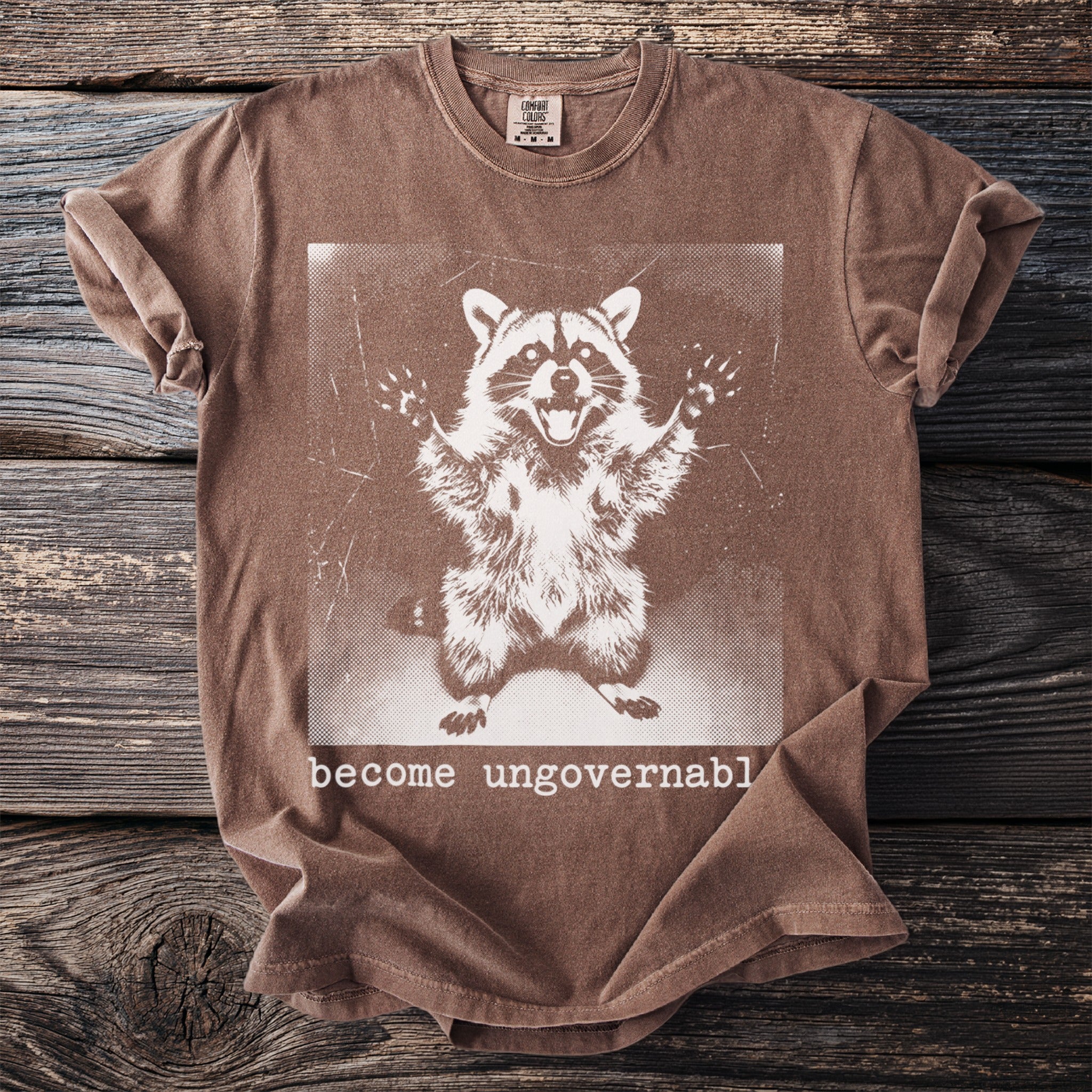 Brown t-shirt with a graphic of a raccoon and text "become ungovernable".
