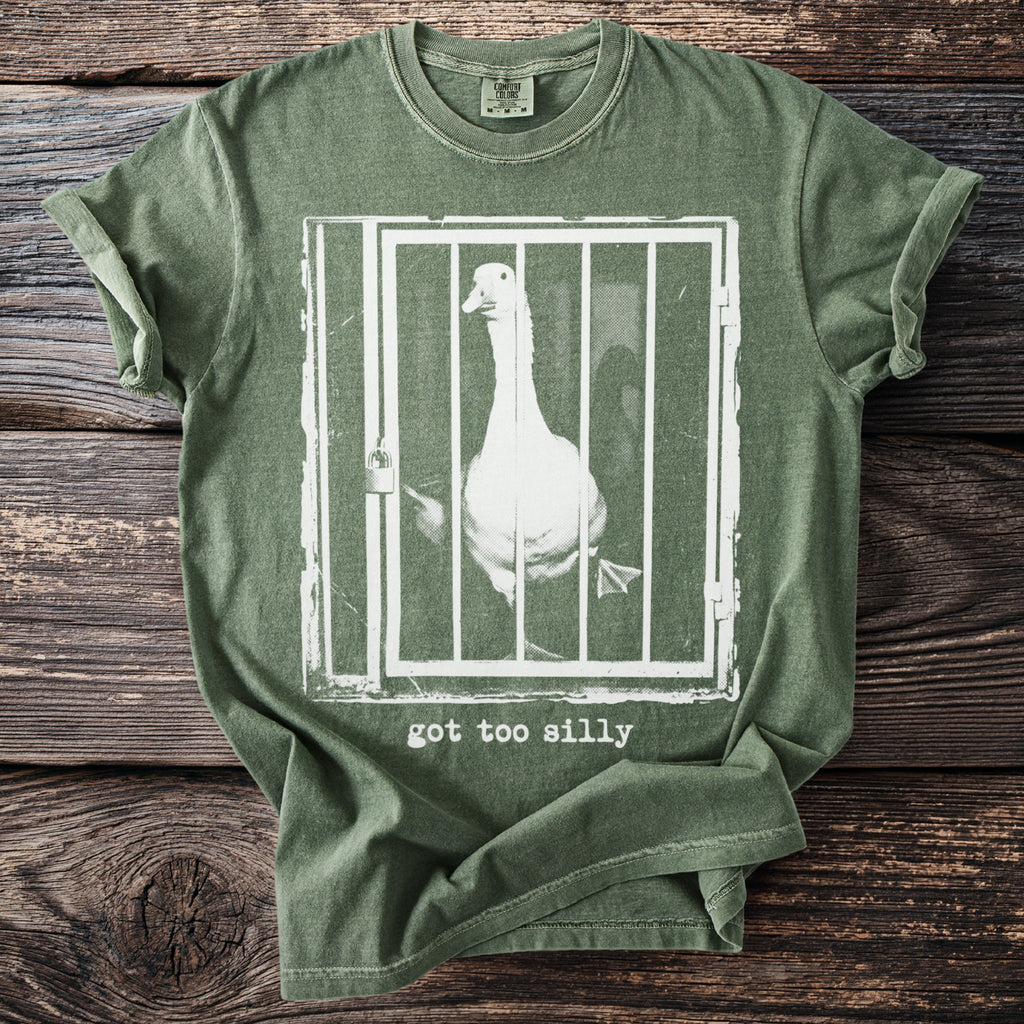 Green t-shirt with white graphic of a goose in a cage and text "got too silly".