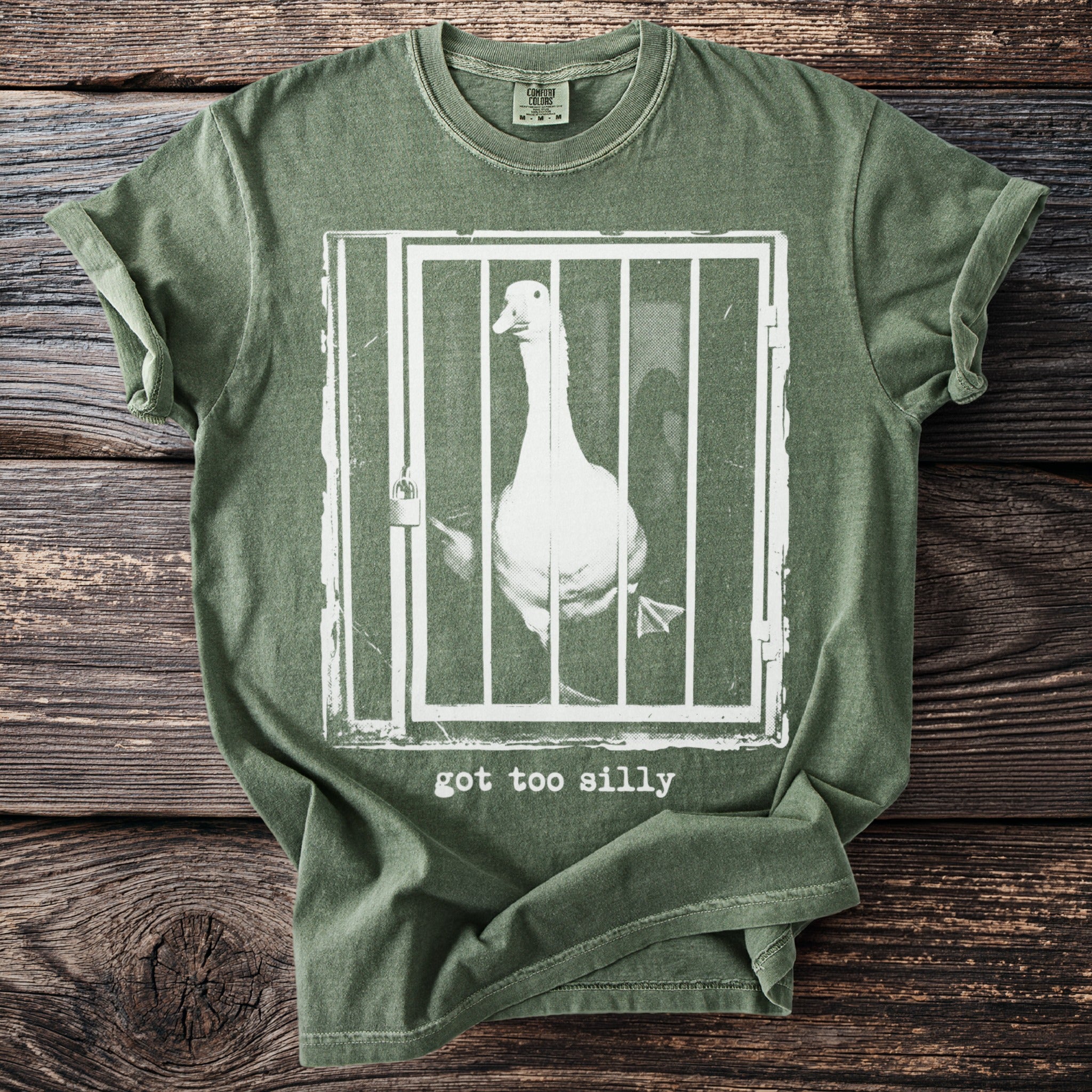 Green t-shirt with white graphic of a goose in a cage and text "got too silly".