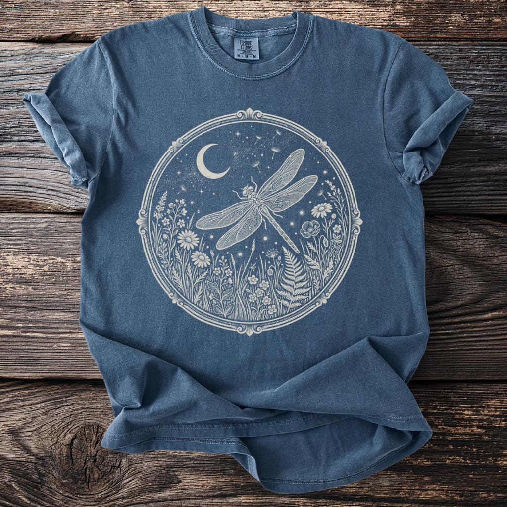 Blue t-shirt with a white oval graphic of a dragonfly and moon over wildflowers.