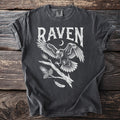 Dark t-shirt with white graphic of a raven in flight above a branch and pinecones.