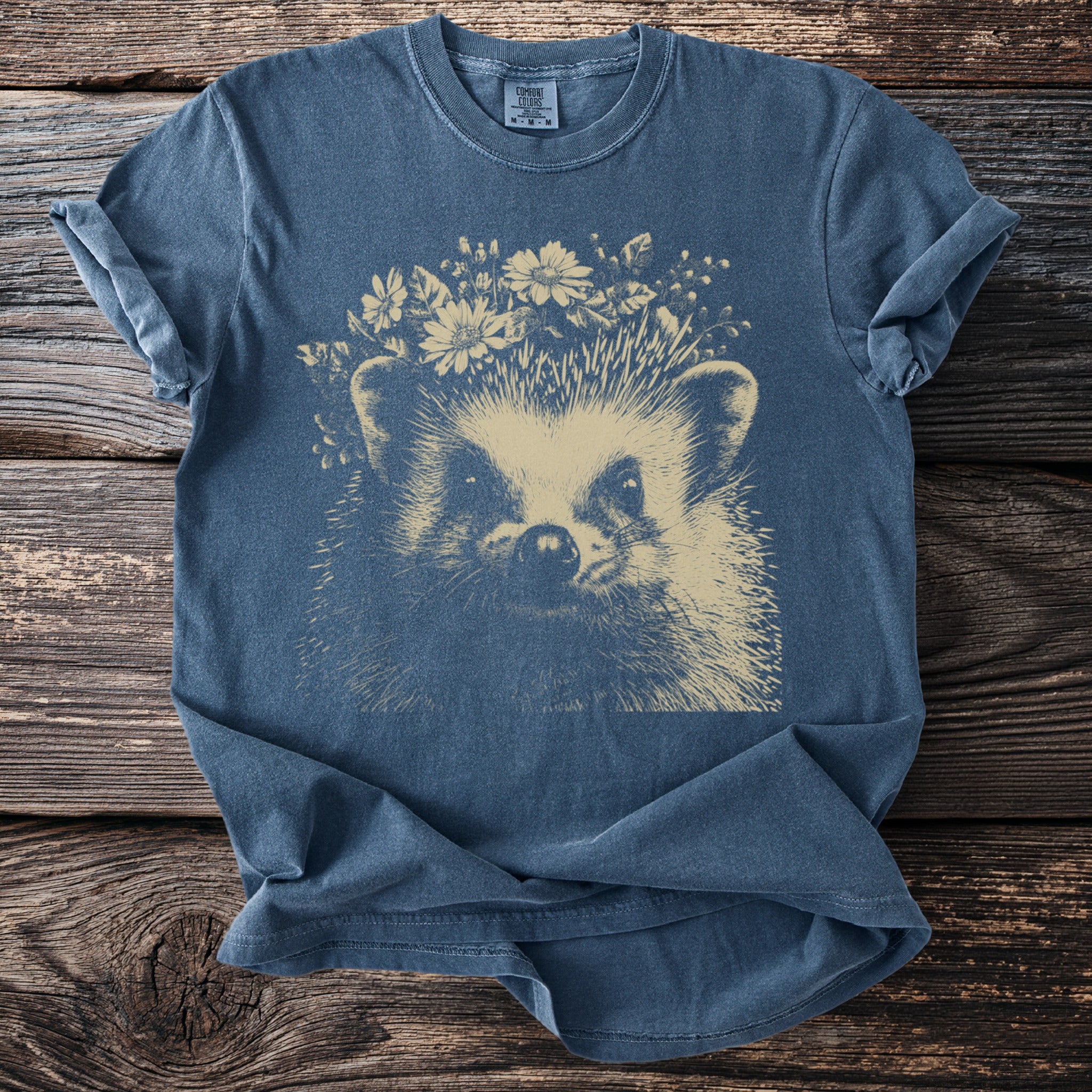 Blue t-shirt with a cream-colored hedgehog wearing a flower crown, Comfort Colors tag.