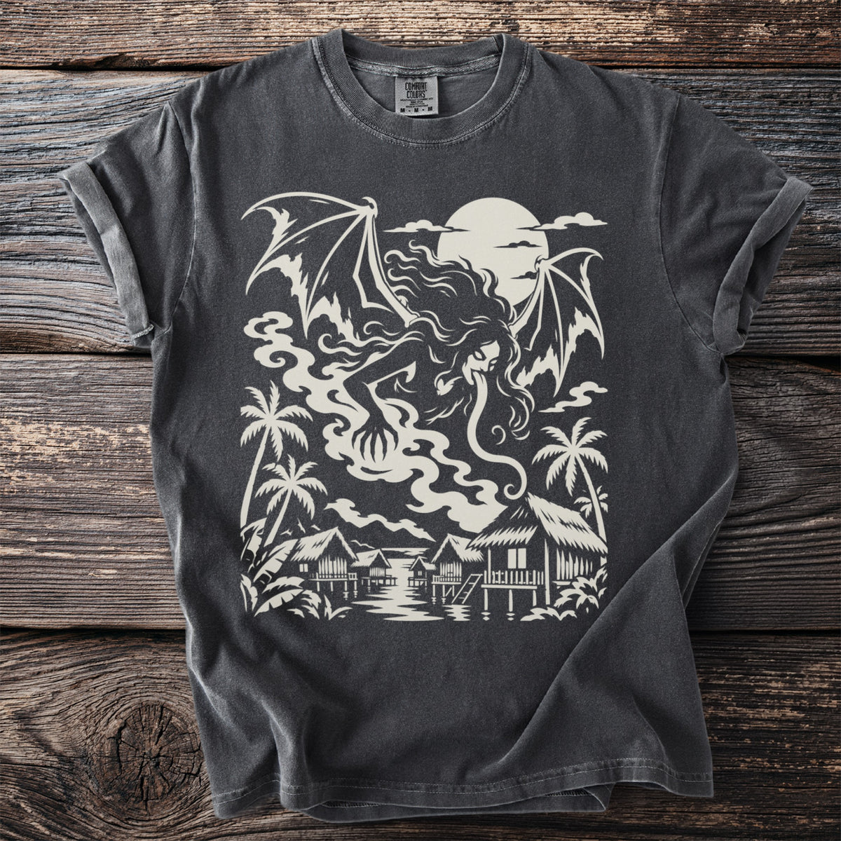Dark grey t-shirt with a white graphic of a winged creature over a tropical village.