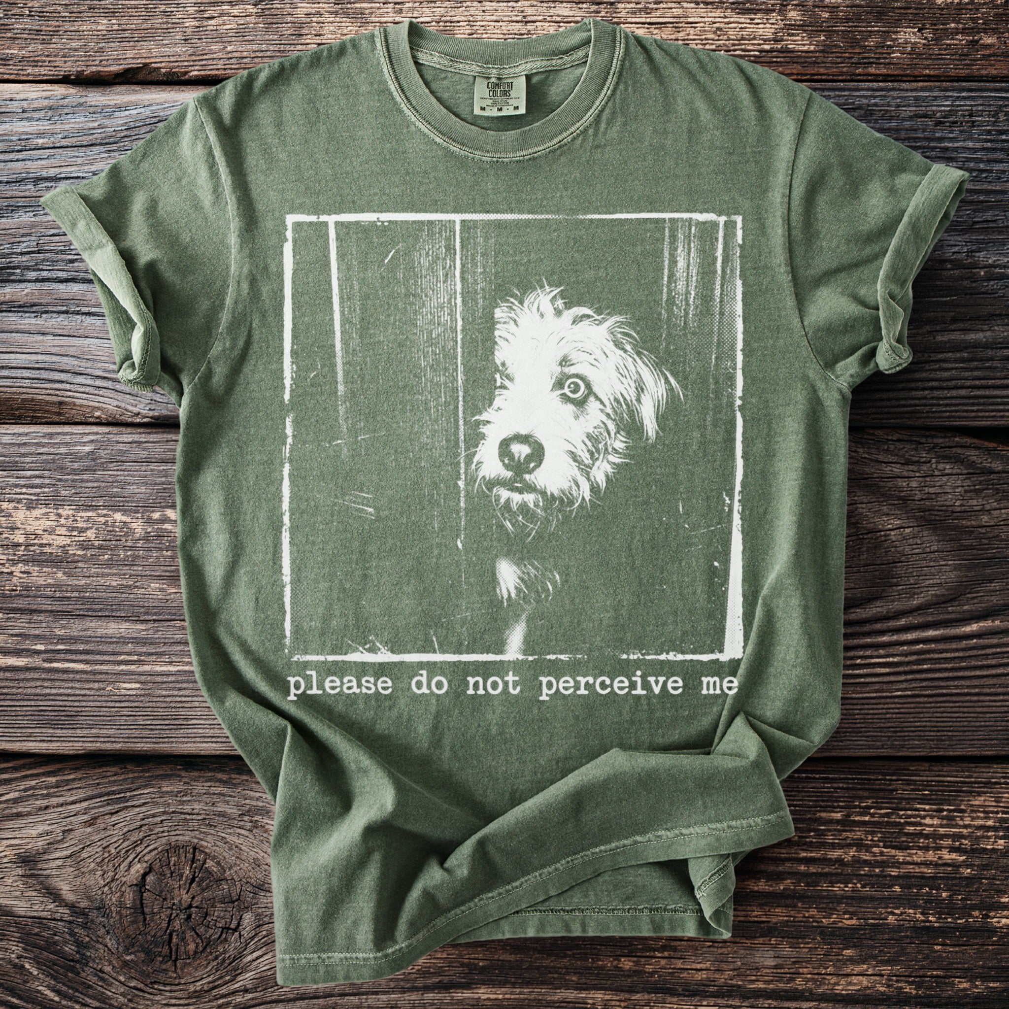 Green t-shirt with a distressed print of a dog peeking out and text saying "please do not perceive me".
