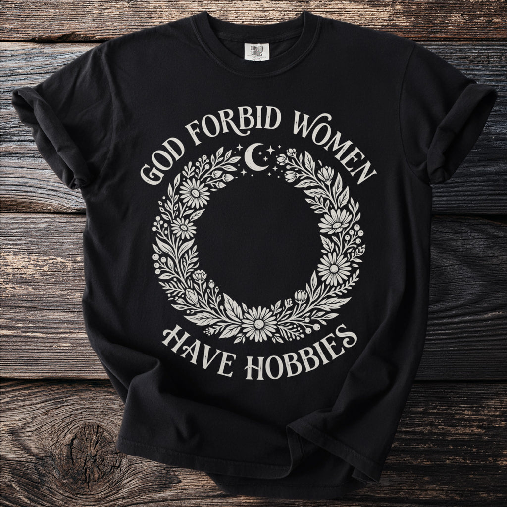 Black t-shirt with floral wreath and text "God Forbid Women Have Hobbies"