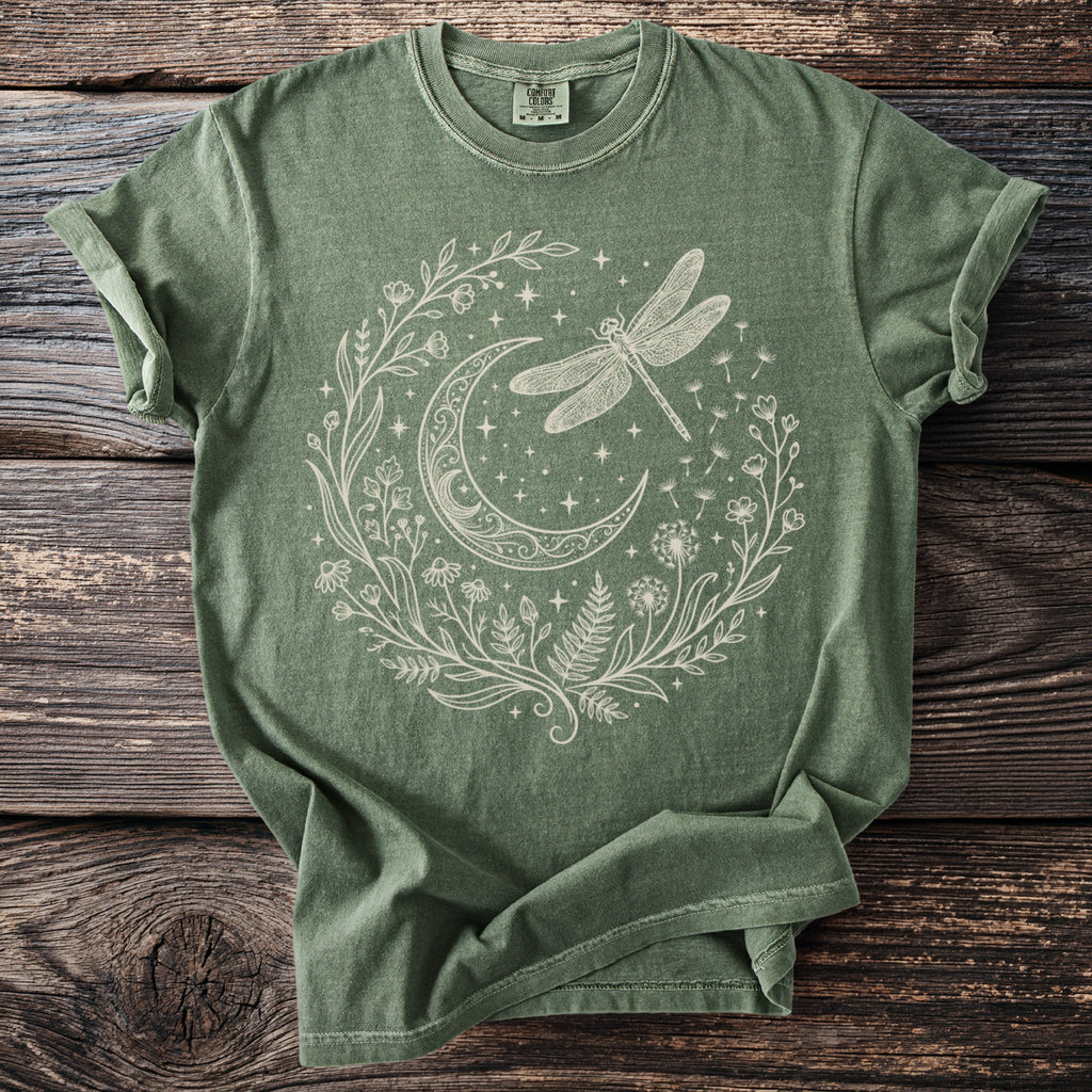 Green t-shirt with cream line art of a dragonfly, moon, and floral wreath.