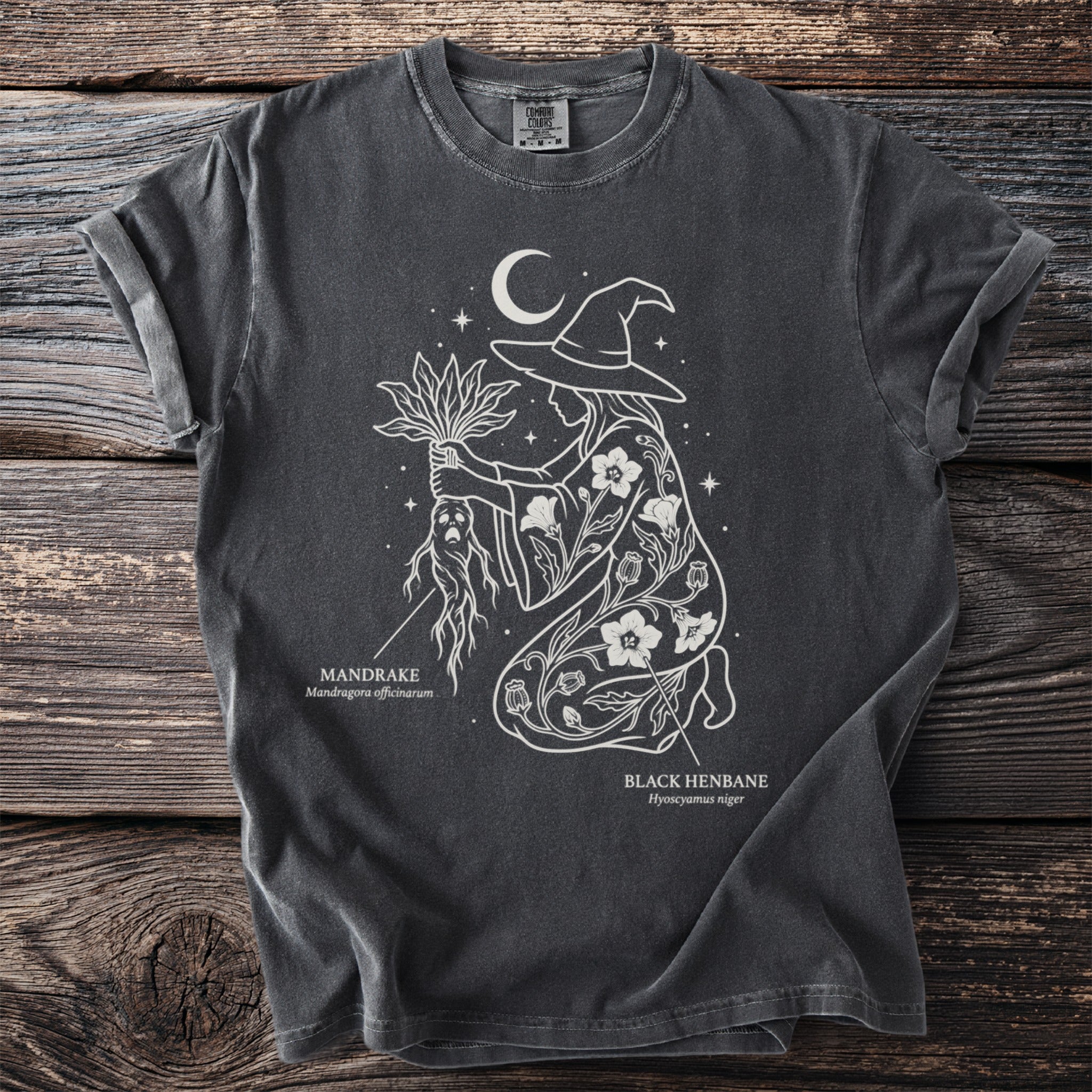 Dark t-shirt with white line art of a witch, mandrake, and black henbane under a moon.