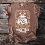 Brown t-shirt with a graphic of a horned devil holding sticks and text "NAUGHTY LIST APPROVED".