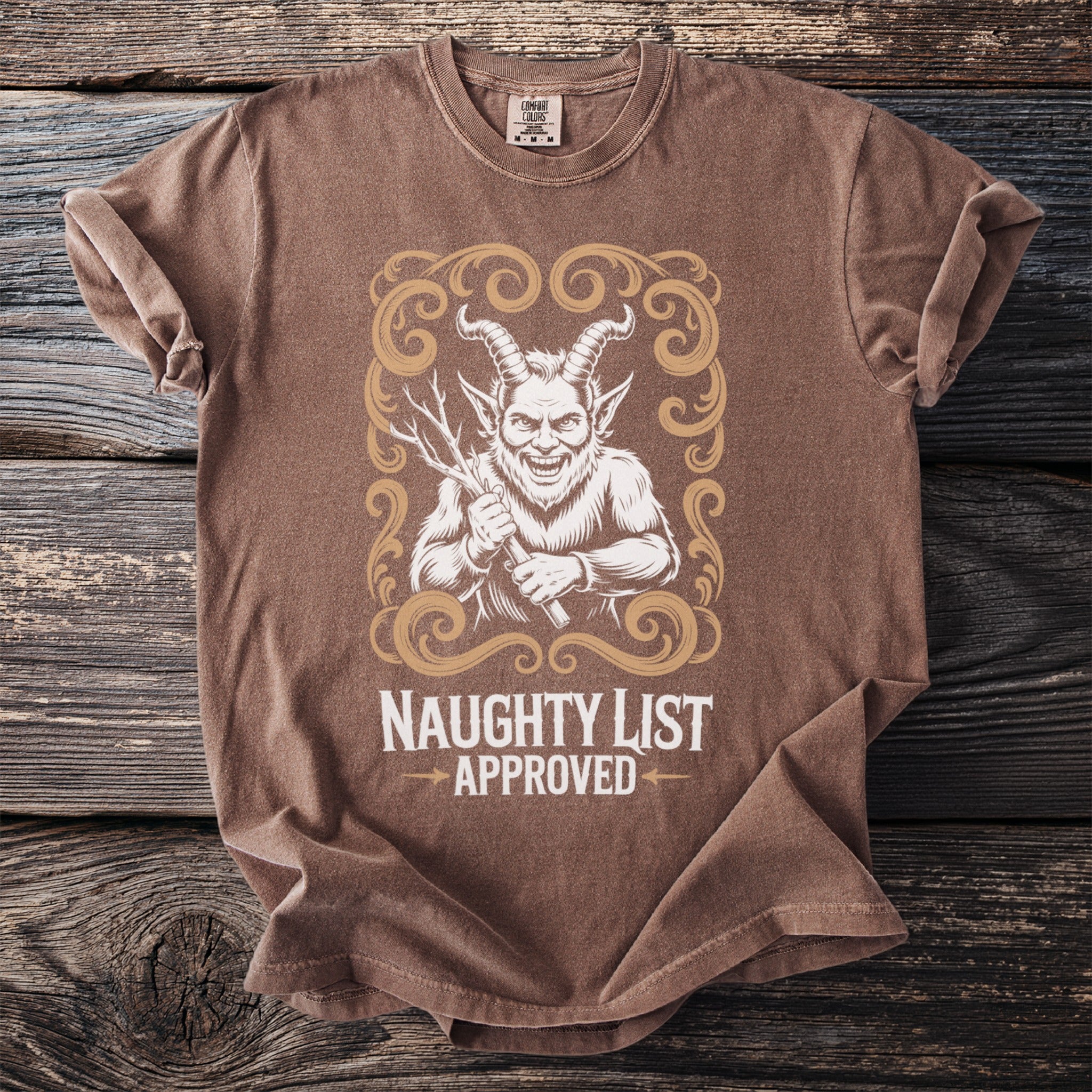 Brown t-shirt with a graphic of a horned devil holding sticks and text "NAUGHTY LIST APPROVED".