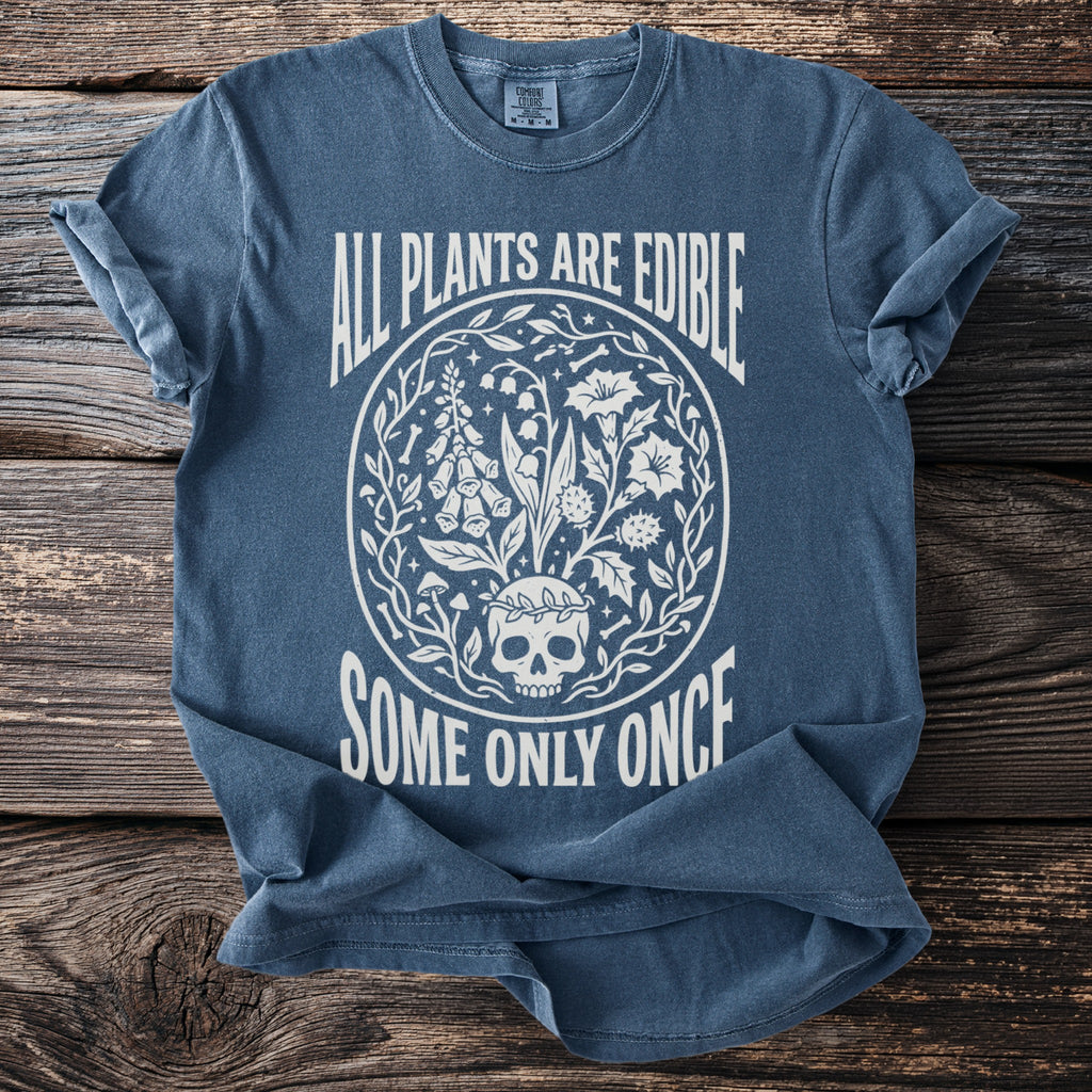 Blue t-shirt with white graphic of a skull, plants, and text "ALL PLANTS ARE EDIBLE SOME ONLY ONCE".
