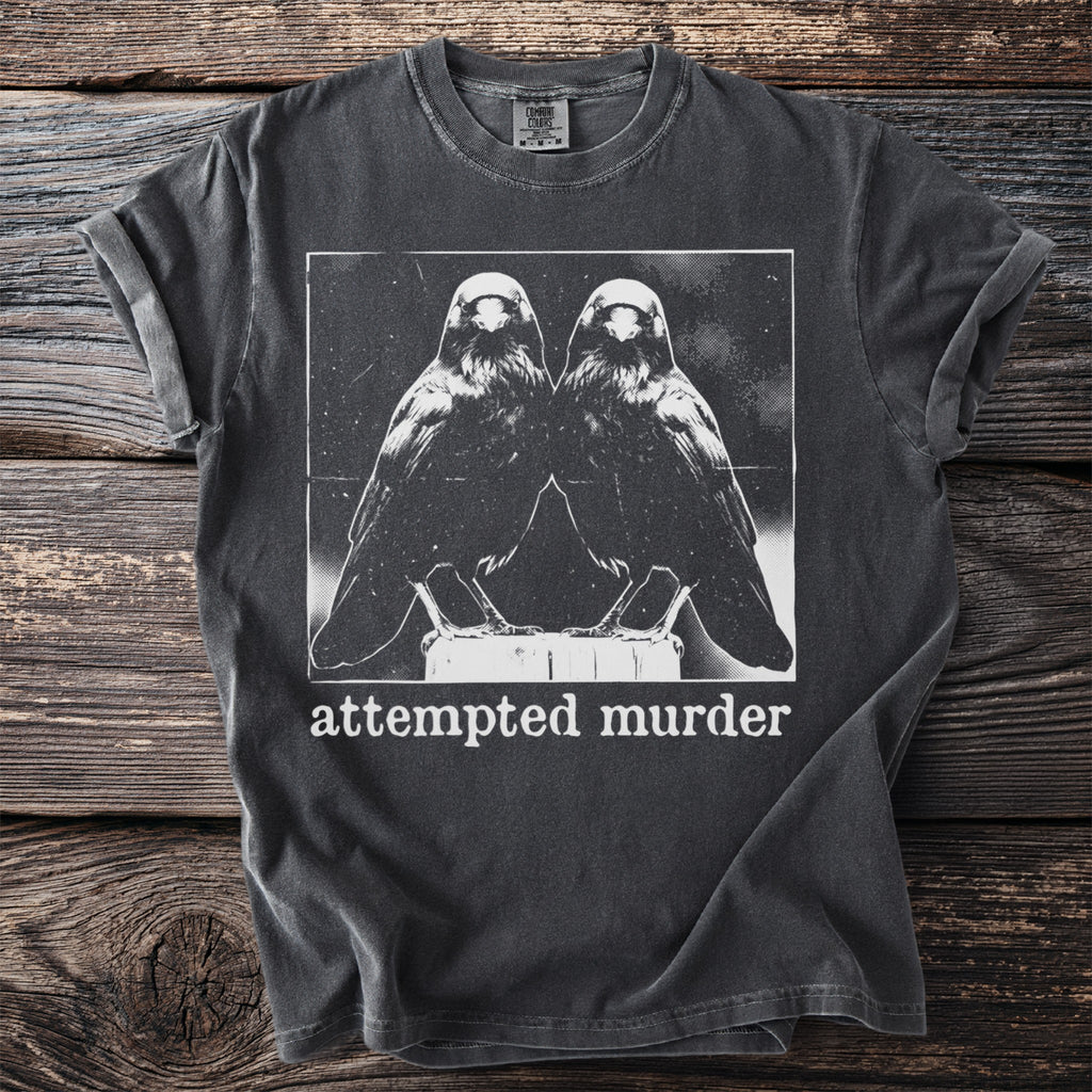 Dark charcoal t-shirt with a white graphic of two ravens and the text "attempted murder".