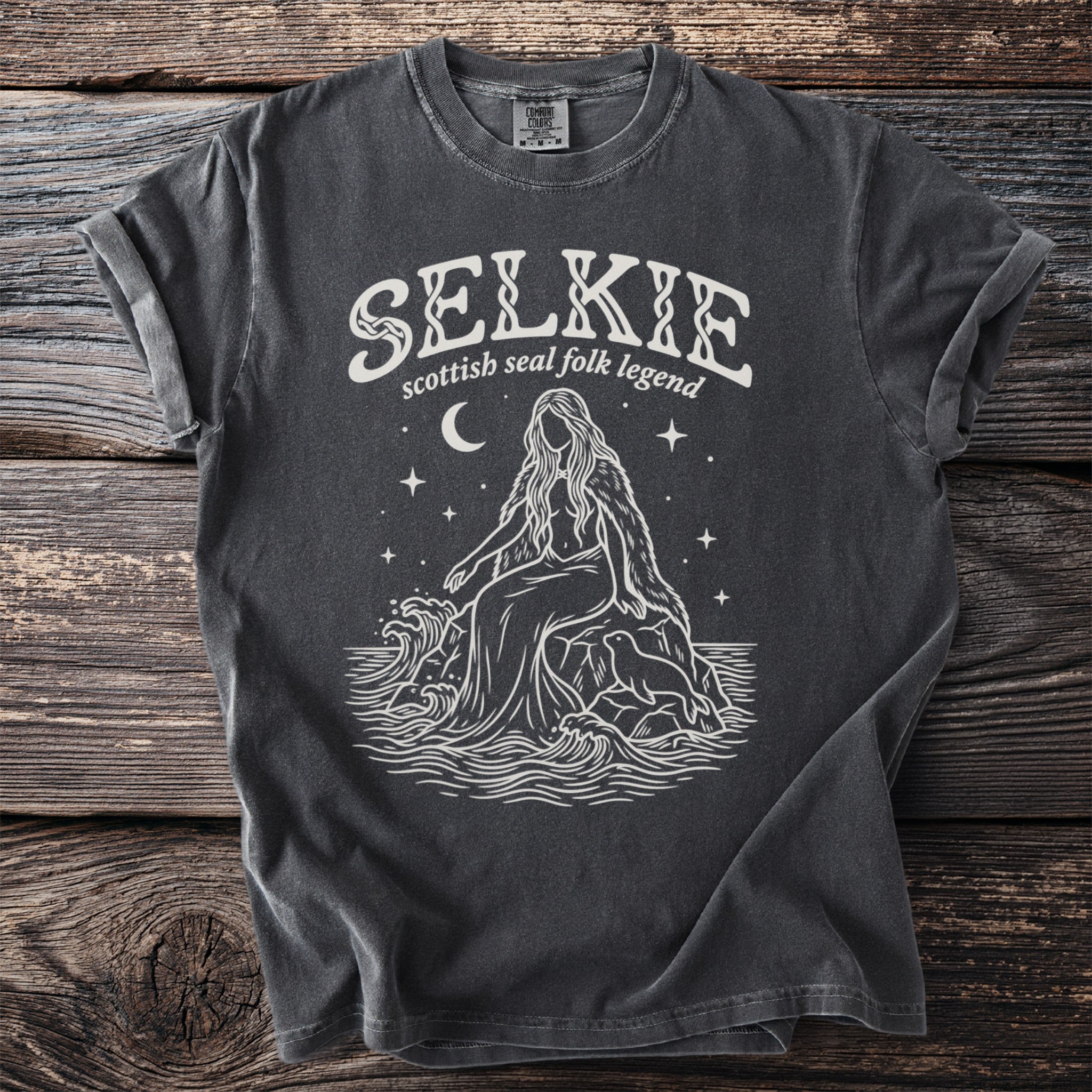 Dark gray t-shirt with white graphic: "SELKIE scottish seal folk legend" above a sitting mythical figure.