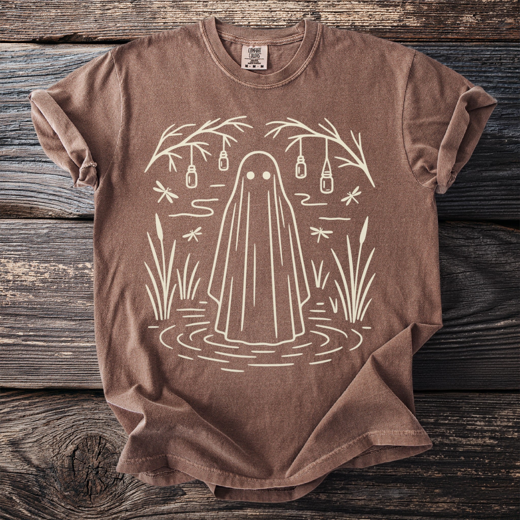 Brown t-shirt with a line drawing of a ghost in water surrounded by reeds and hanging jars.
