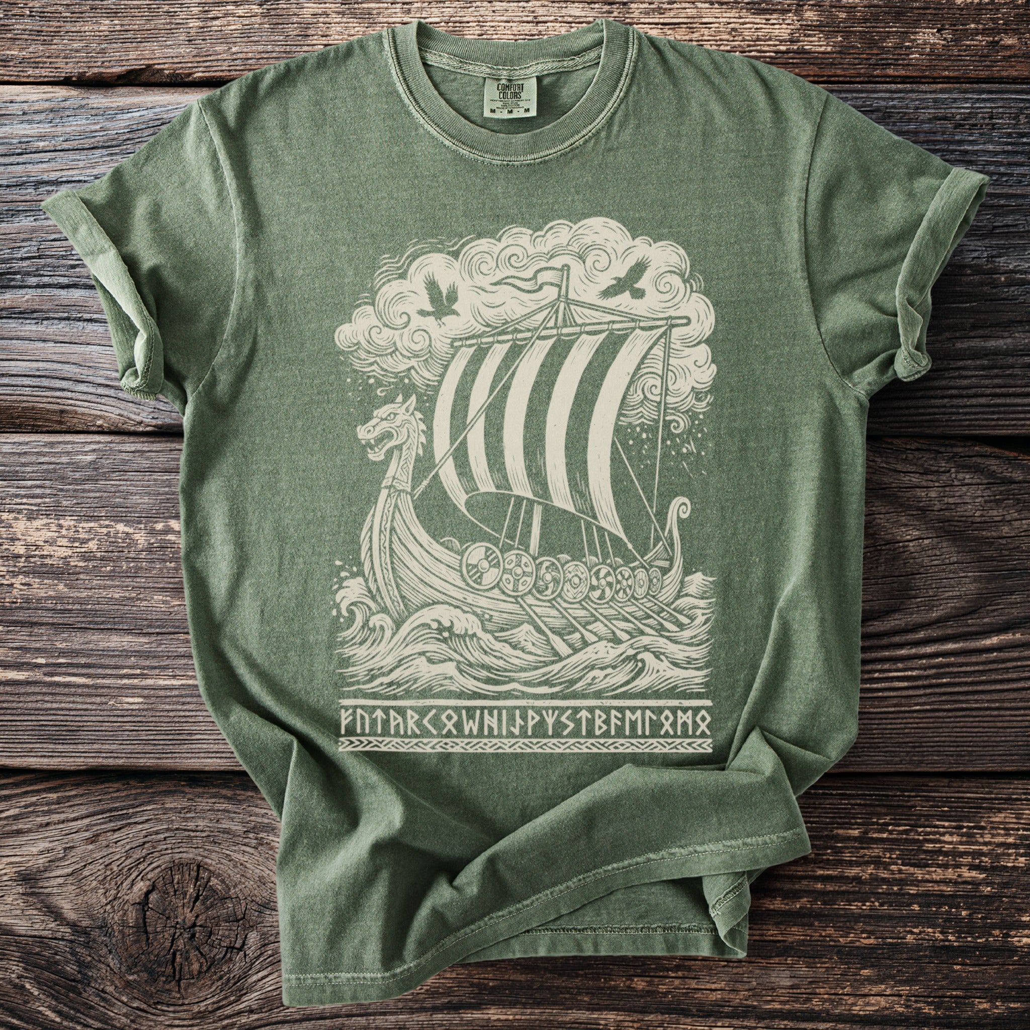Green t-shirt with a cream graphic of a Viking ship, birds, and runes.