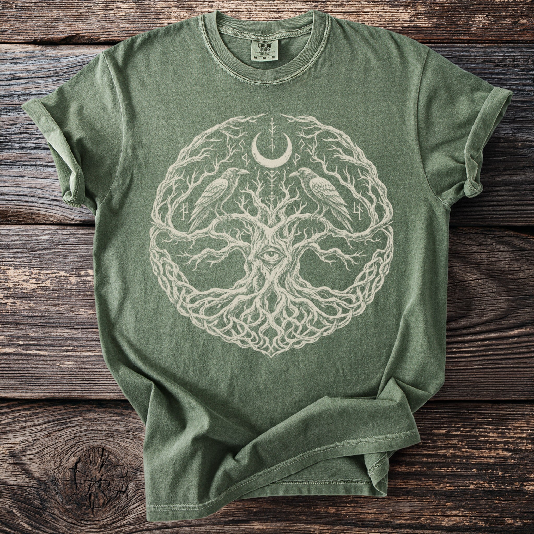 Olive green t-shirt with a central circular design of a tree, eye, moon, and ravens.