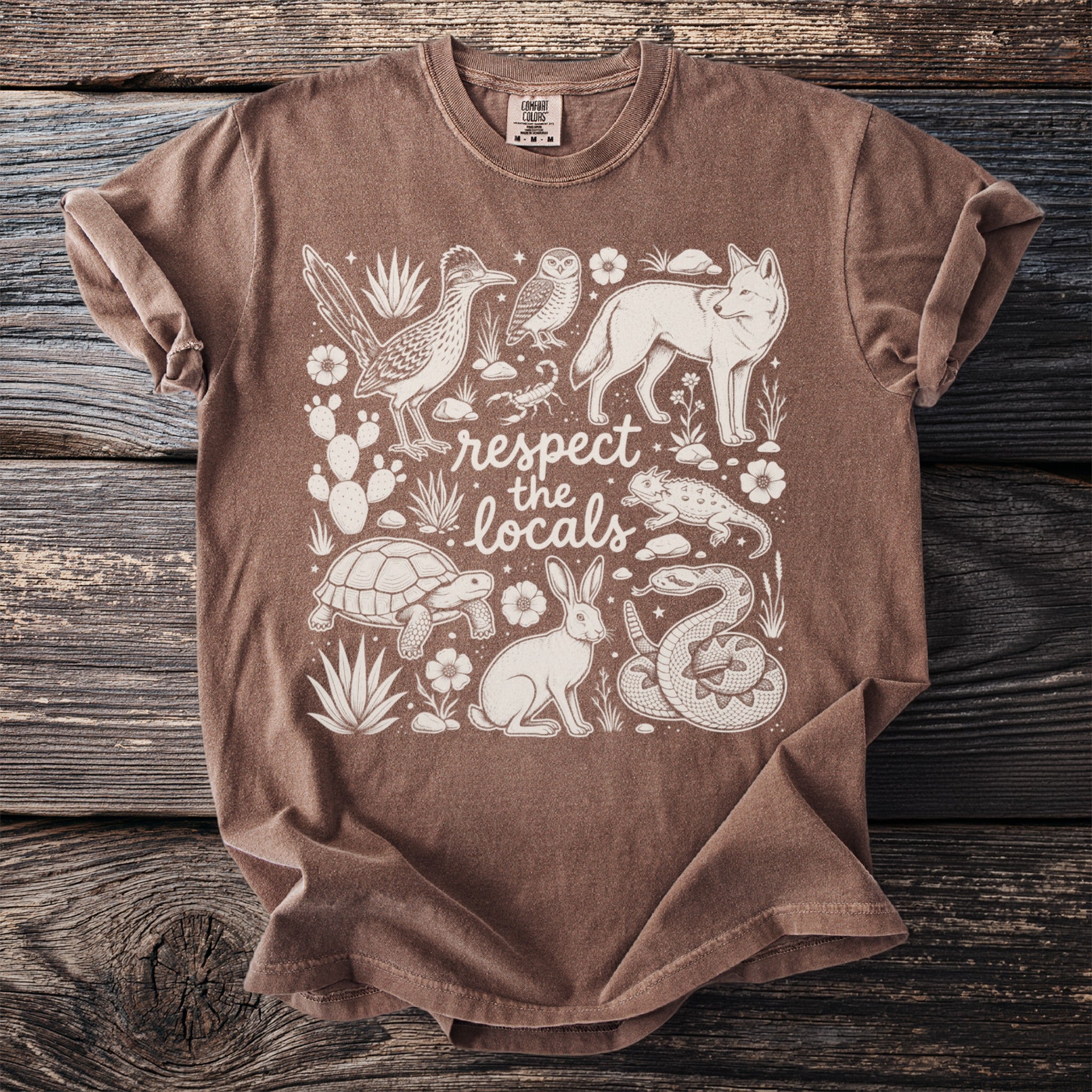 Brown t-shirt with white line art of desert animals and plants and text "respect the locals".