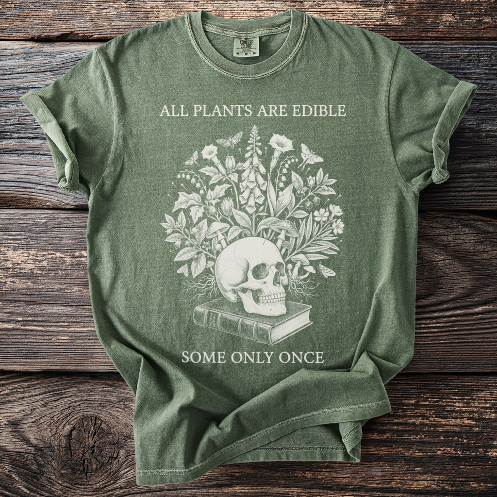Green t-shirt with skull, plants, mushrooms, book, and text "ALL PLANTS ARE EDIBLE SOME ONLY ONCE".