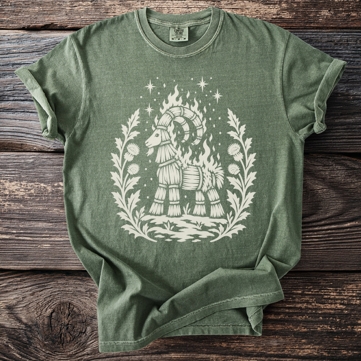 Green t-shirt with cream design of a straw goat on fire within a floral wreath.