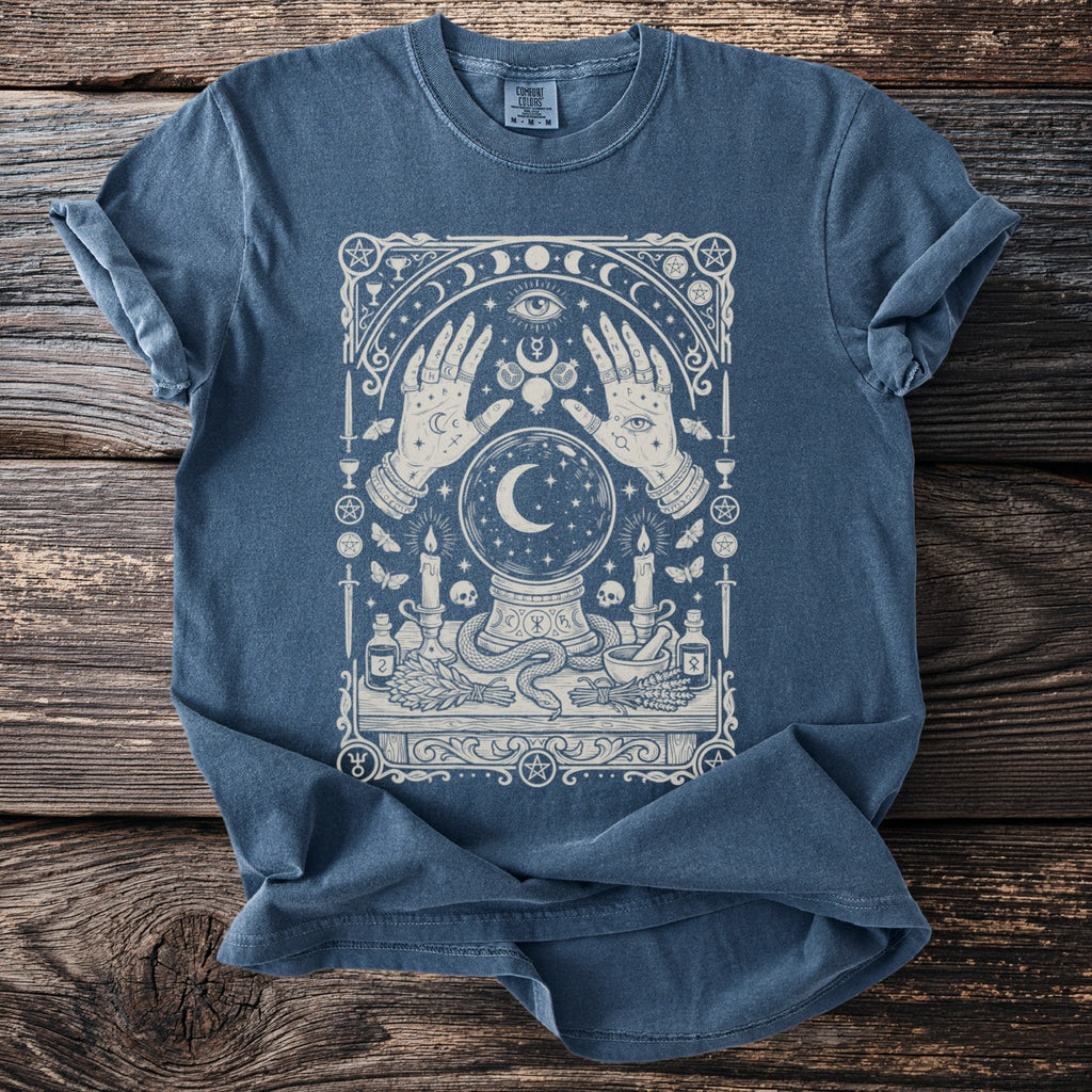 Blue t-shirt with mystical illustration of hands, crystal ball, moon, candles and occult symbols.