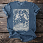 Blue t-shirt with mystical illustration of hands, crystal ball, moon, candles and occult symbols.