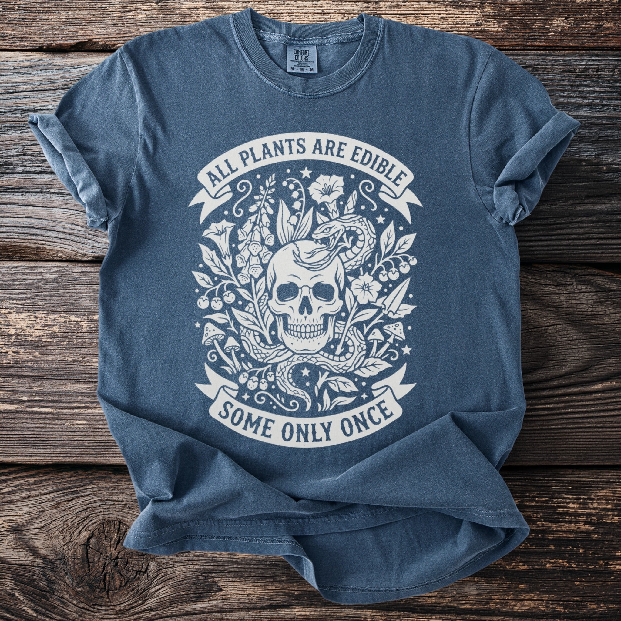Blue t-shirt with a skull, snake, and plants design that reads "All plants are edible, some only once".