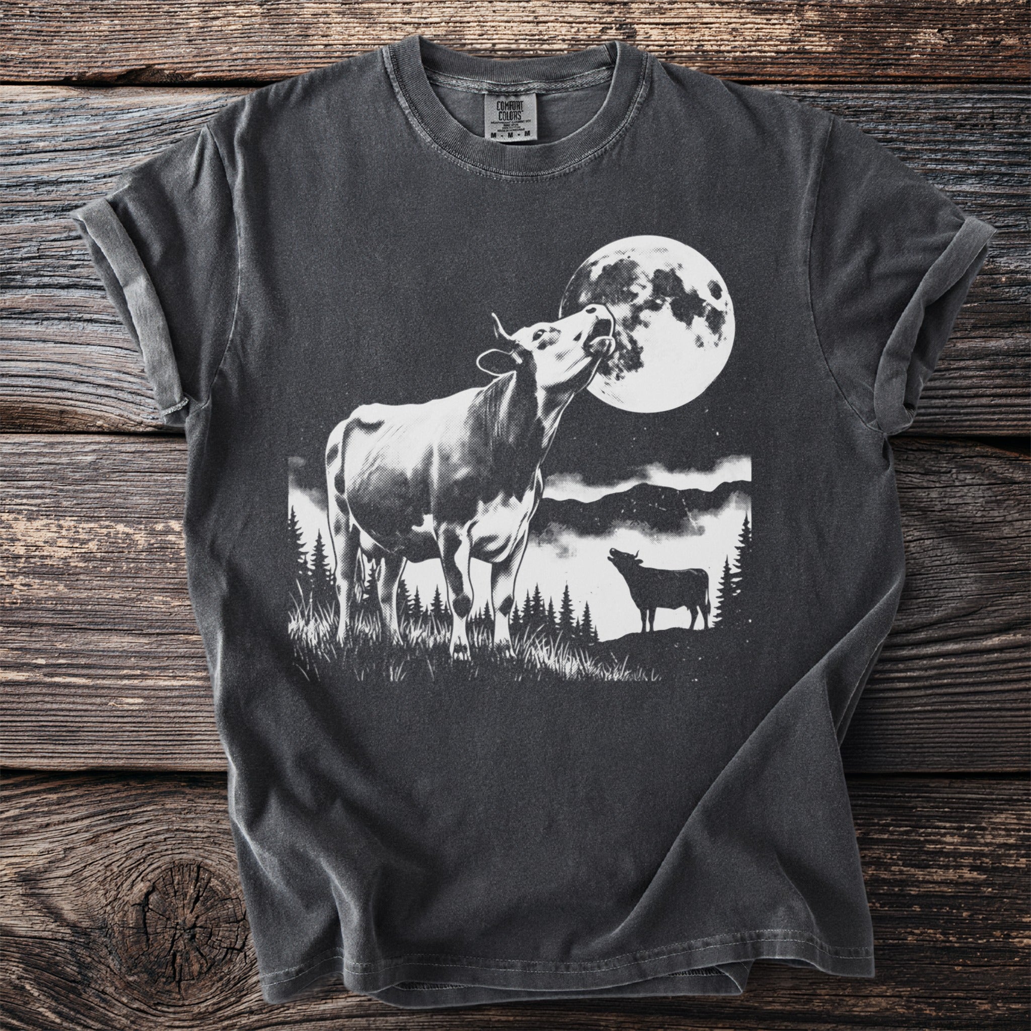 Dark t-shirt with a black and white graphic of cows under a large full moon.