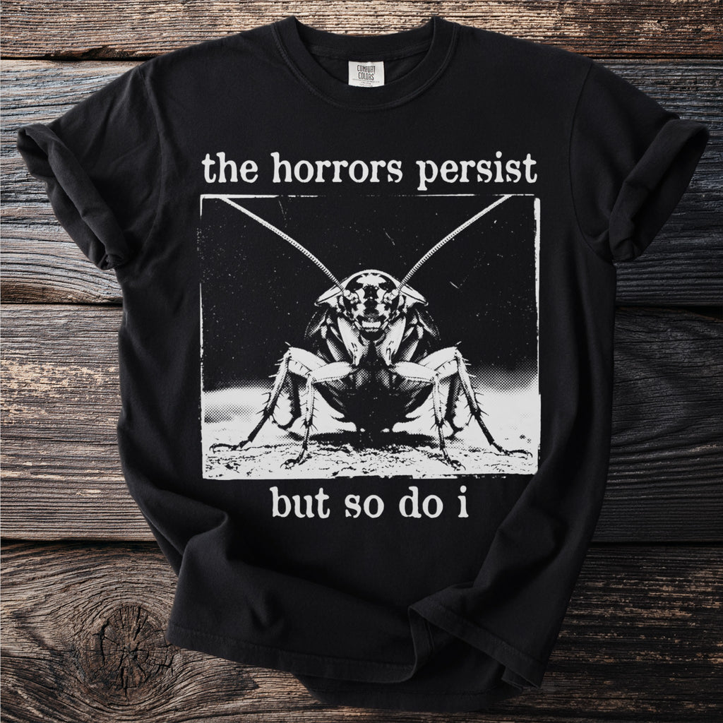 Black t-shirt with a cockroach graphic and text "the horrors persist but so do i".