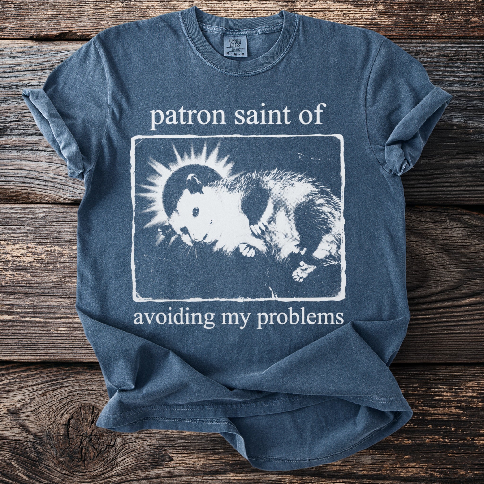 Blue t-shirt with "patron saint of avoiding my problems" and a opossum graphic.