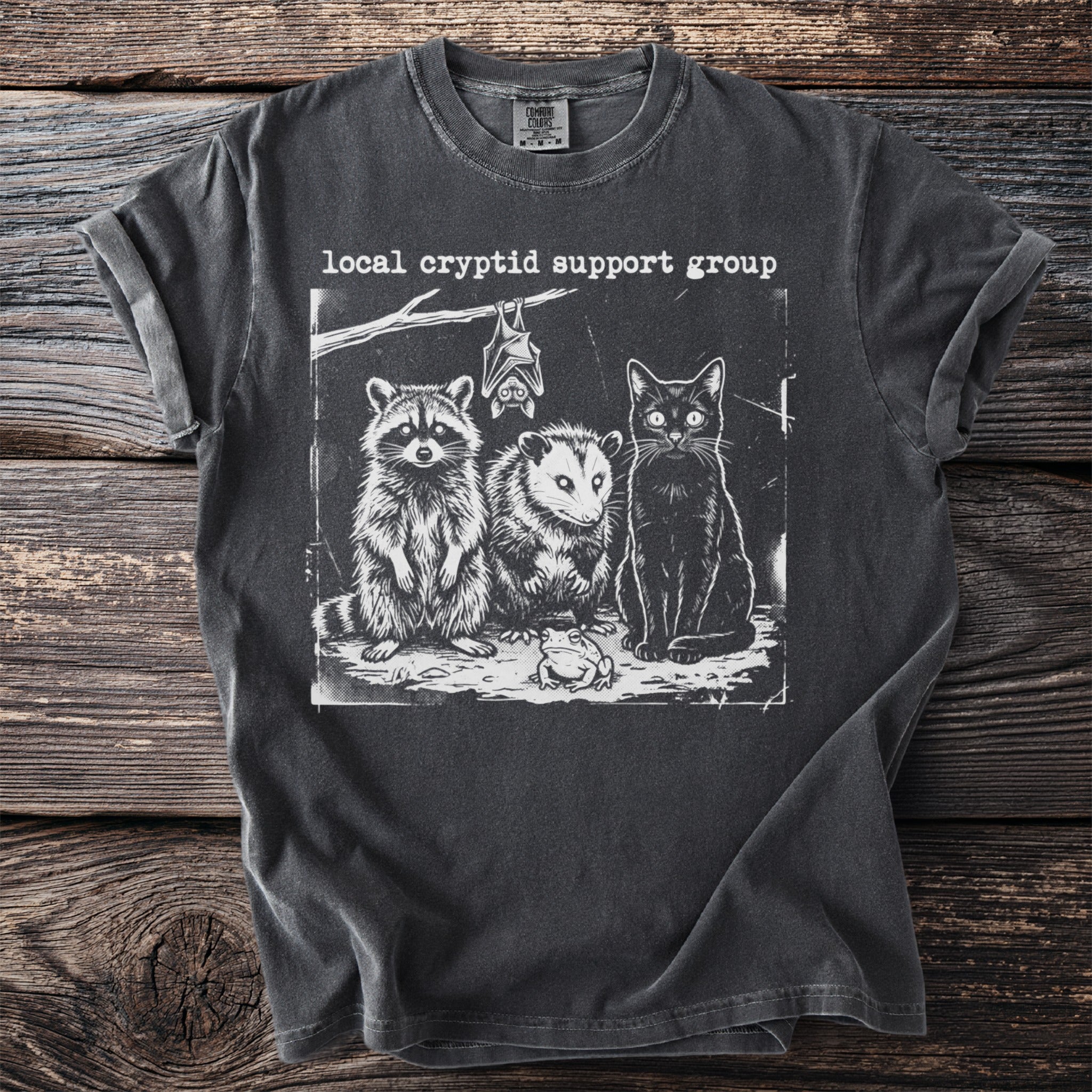 Dark grey Comfort Colors t-shirt with "Local Cryptid Support Group" text and graphic of raccoon, opossum, bat, cat, and frog.