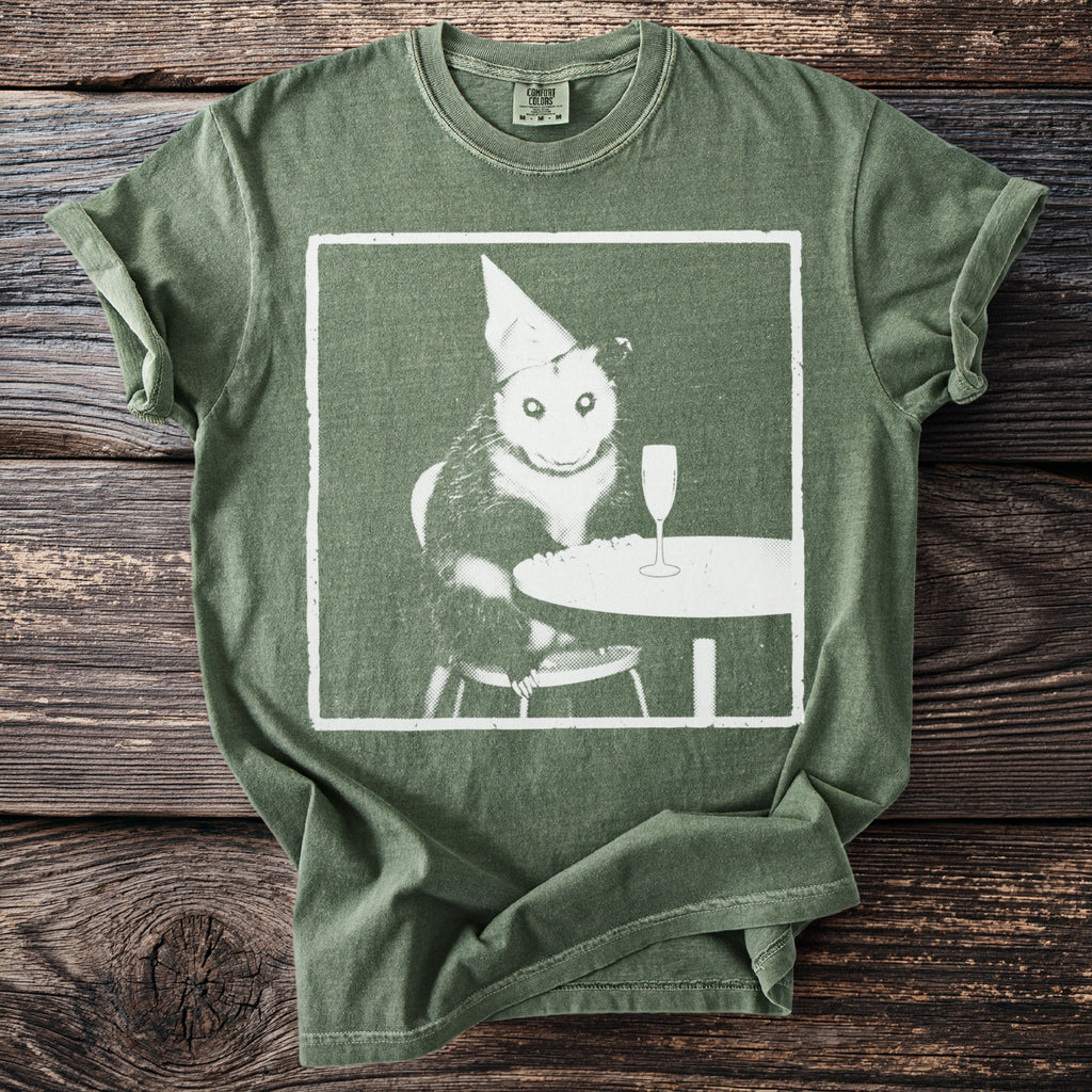 T-shirt with an opossum wearing a party hat at a table with champagne.