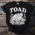 Black t-shirt with white distressed text "TOAD" and a toad illustration with mushrooms and insects.