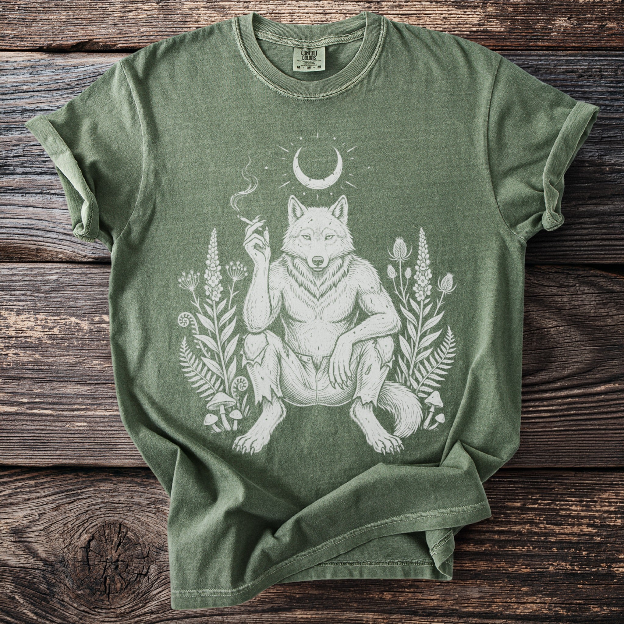 Green t-shirt with a white illustration of a werewolf sitting among plants and mushrooms.